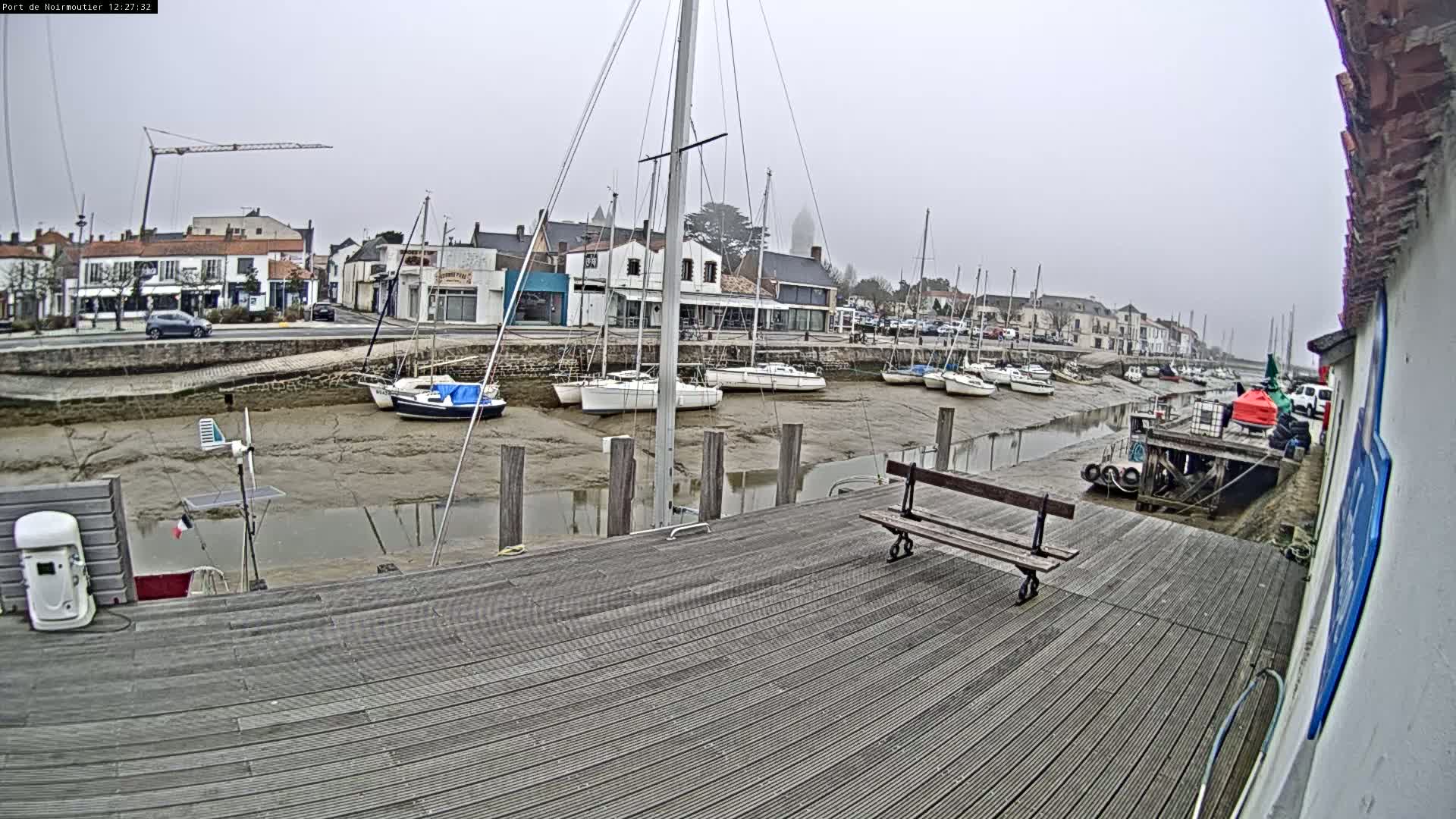 A wooden dock overlooks a harbor with several sailboats at low tide under an overcast sky.