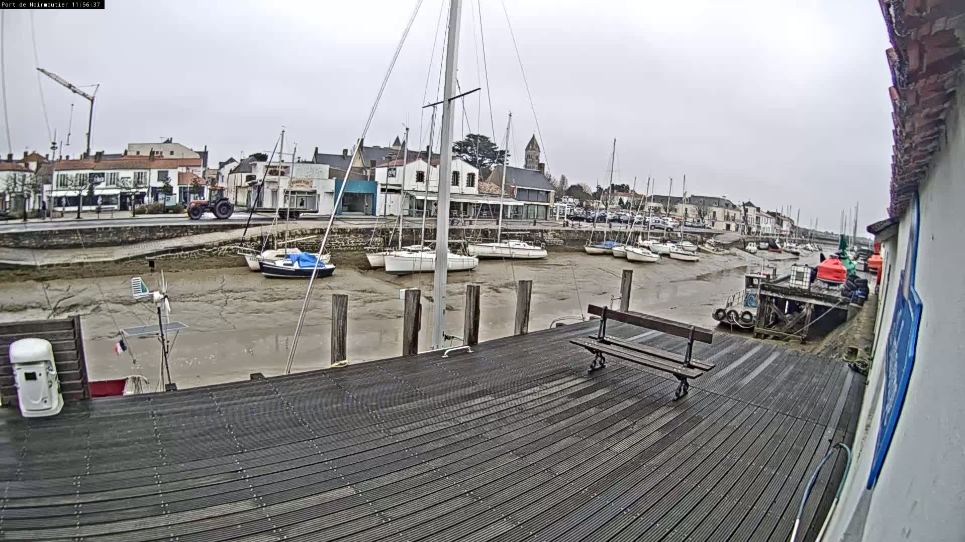 A wooden dock overlooks a harbor with several sailboats at low tide under an overcast sky.