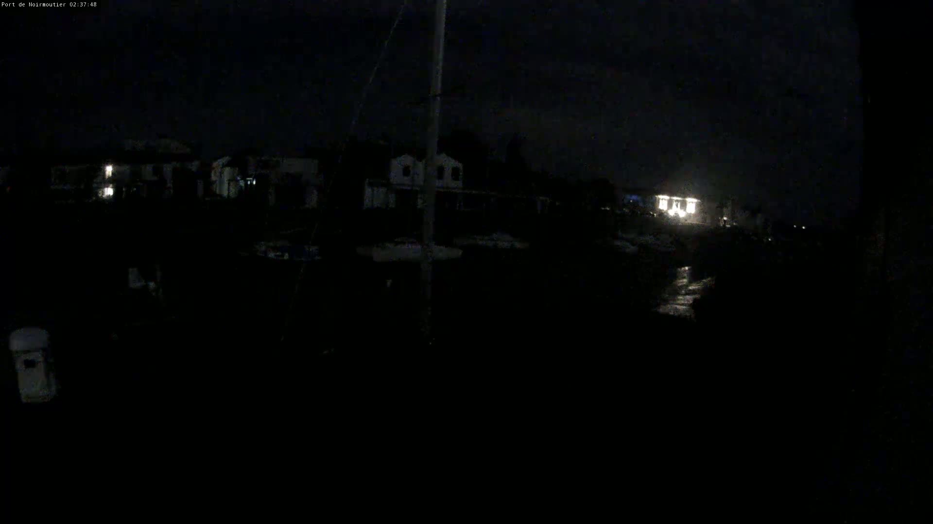 A dark nighttime scene shows dimly lit buildings and what appears to be a boat mast, possibly in a marina.