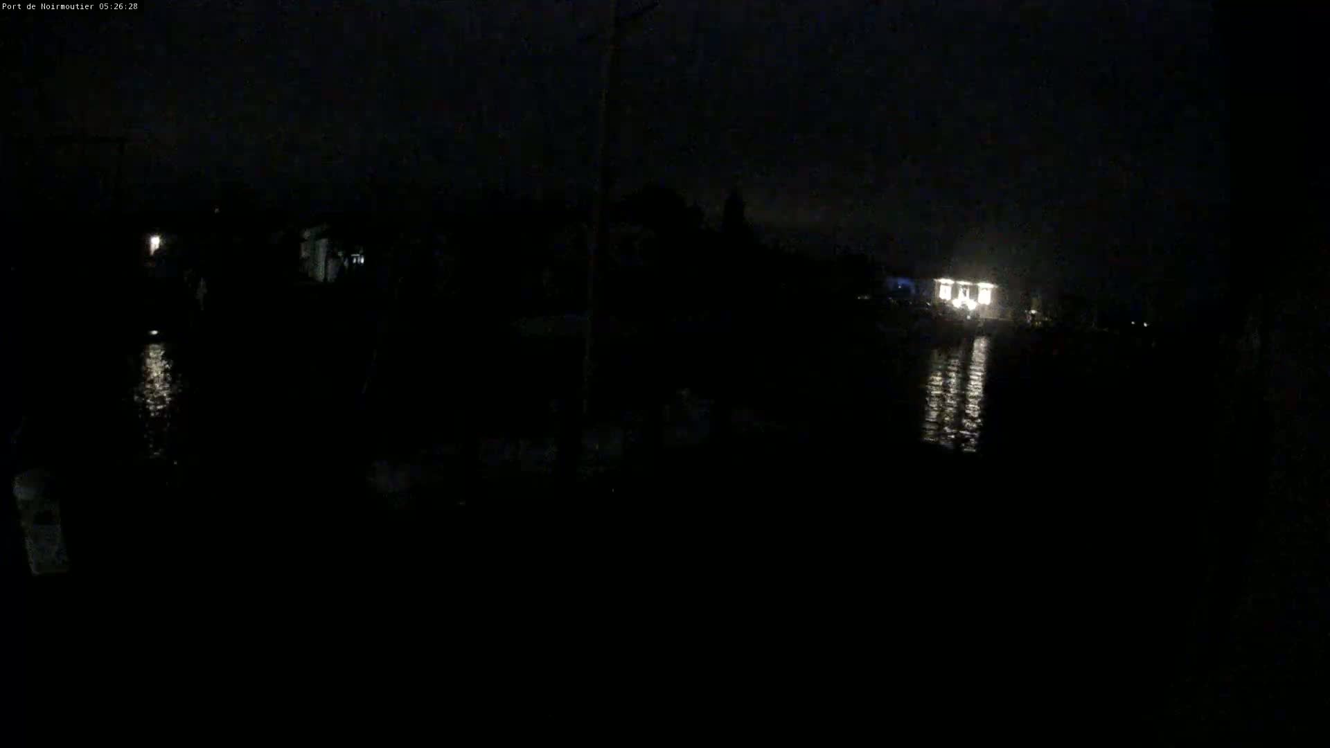 A dark nighttime scene shows a body of water reflecting the lights of a building in the distance.