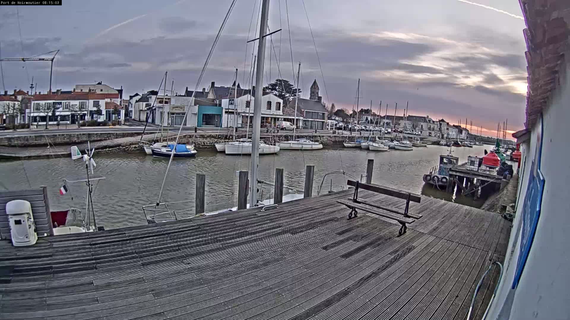 A wooden dock overlooks a calm harbor filled with sailboats and small vessels, under a cloudy, dusky sky.