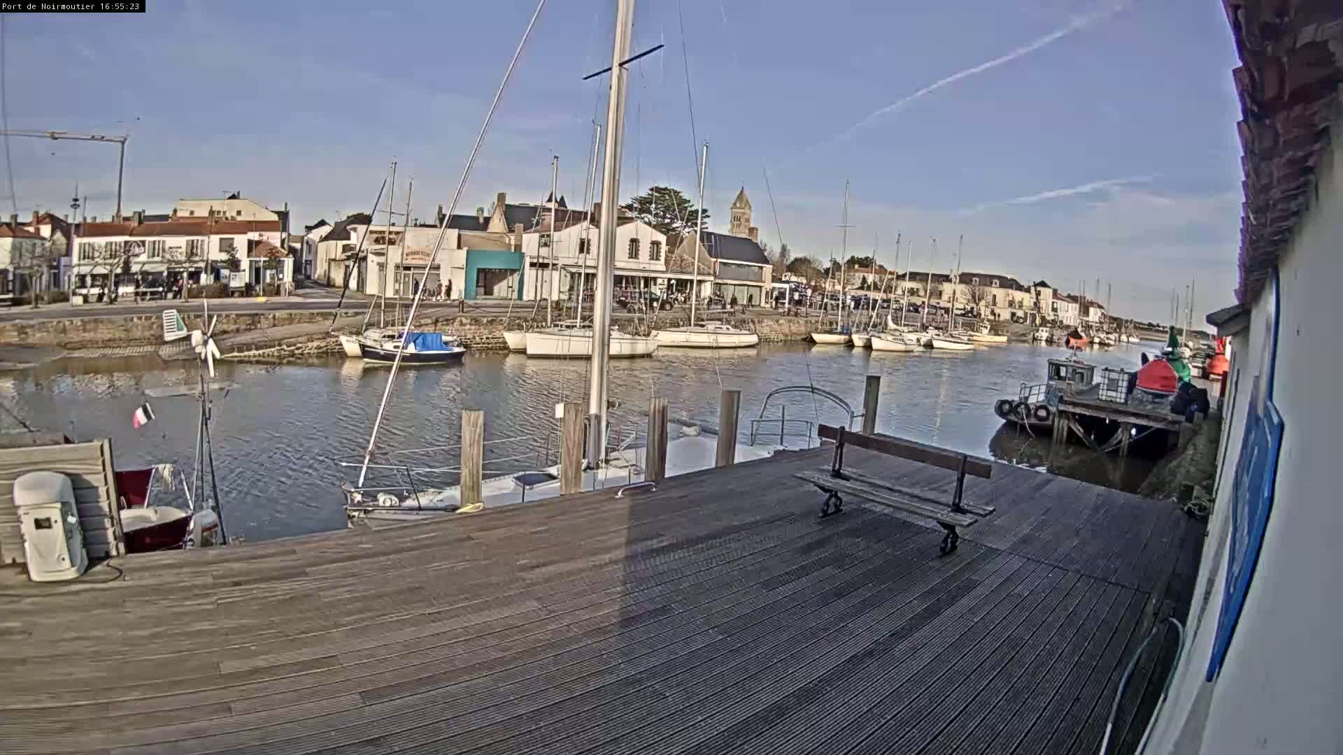 A harbor filled with sailboats is viewed from a wooden dock on a sunny day.