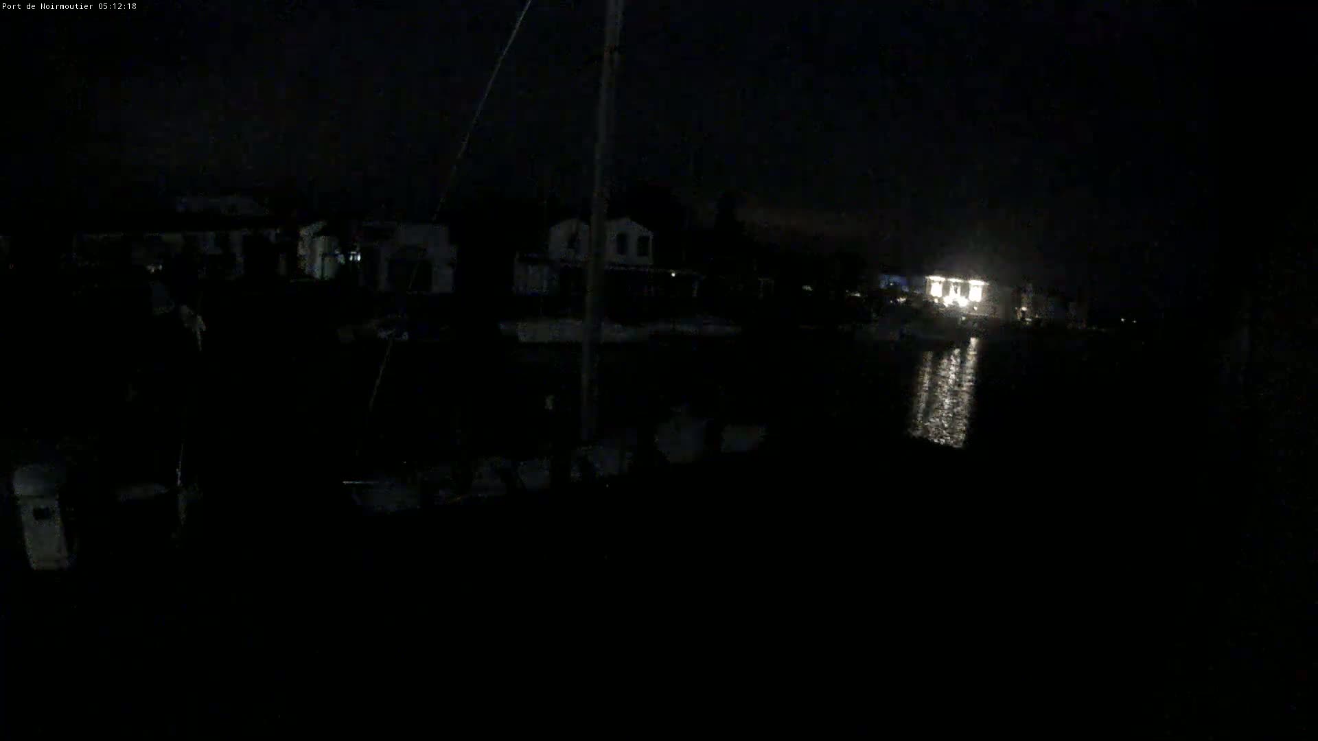 A nighttime view of a dark harbor with dimly lit buildings and boats reflecting light on the water.