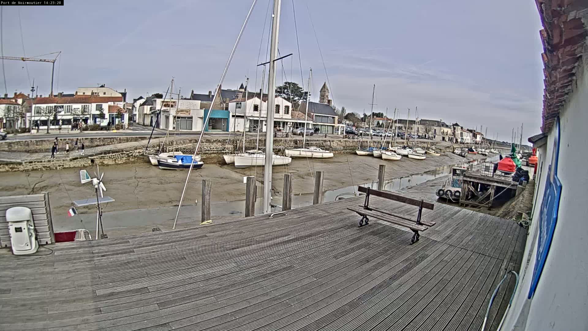 A wooden dock overlooks a harbor with sailboats at low tide under an overcast sky.