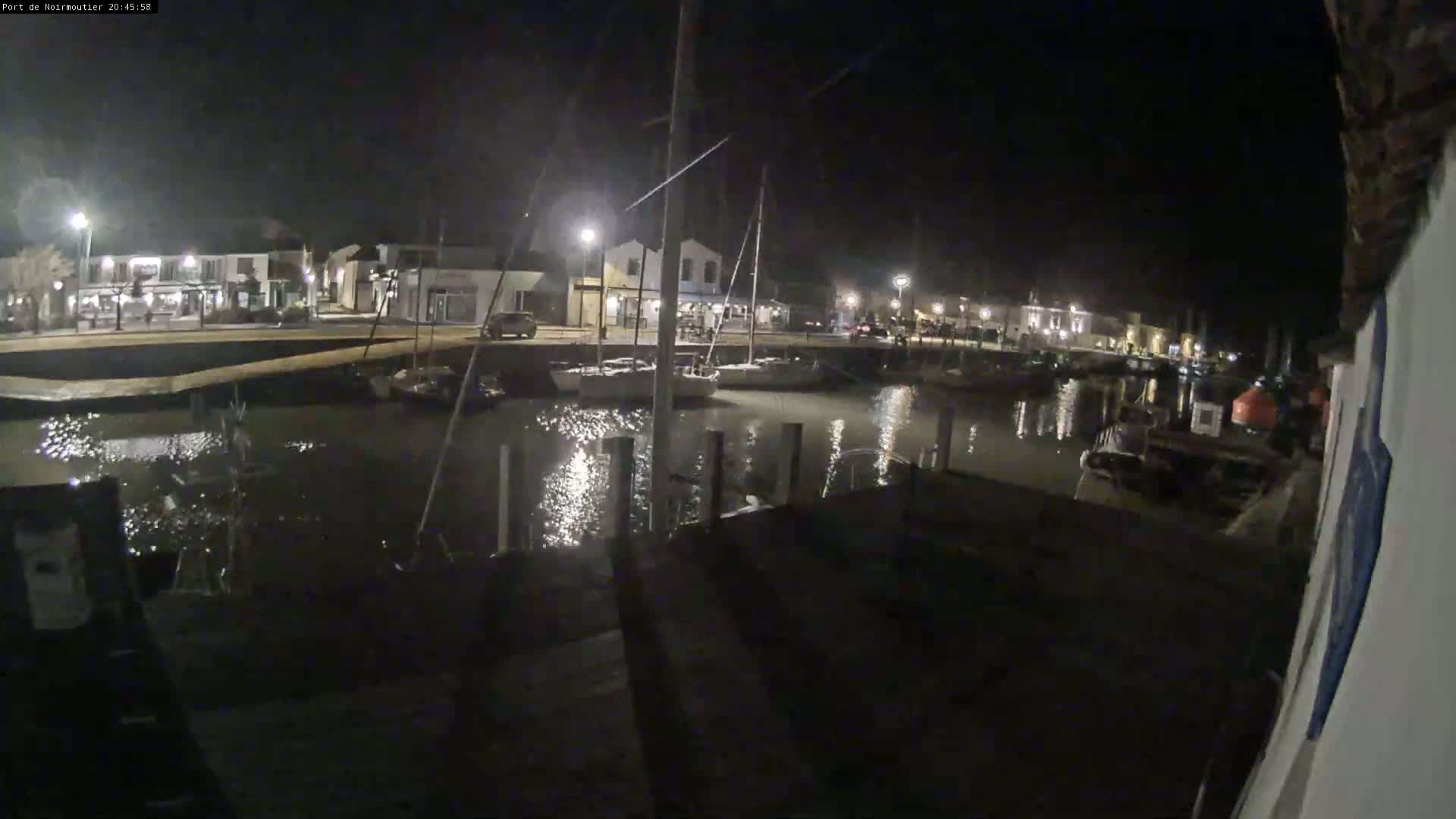 A nighttime view of a calm harbor with boats docked along a waterfront lined with buildings under artificial light.