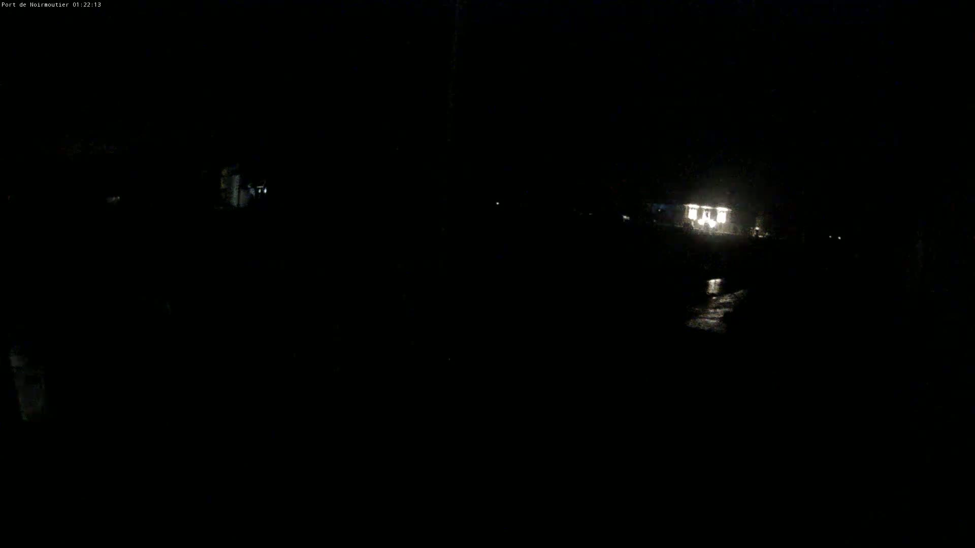 A dimly lit, nighttime scene shows a building with lights on near a dark body of water.