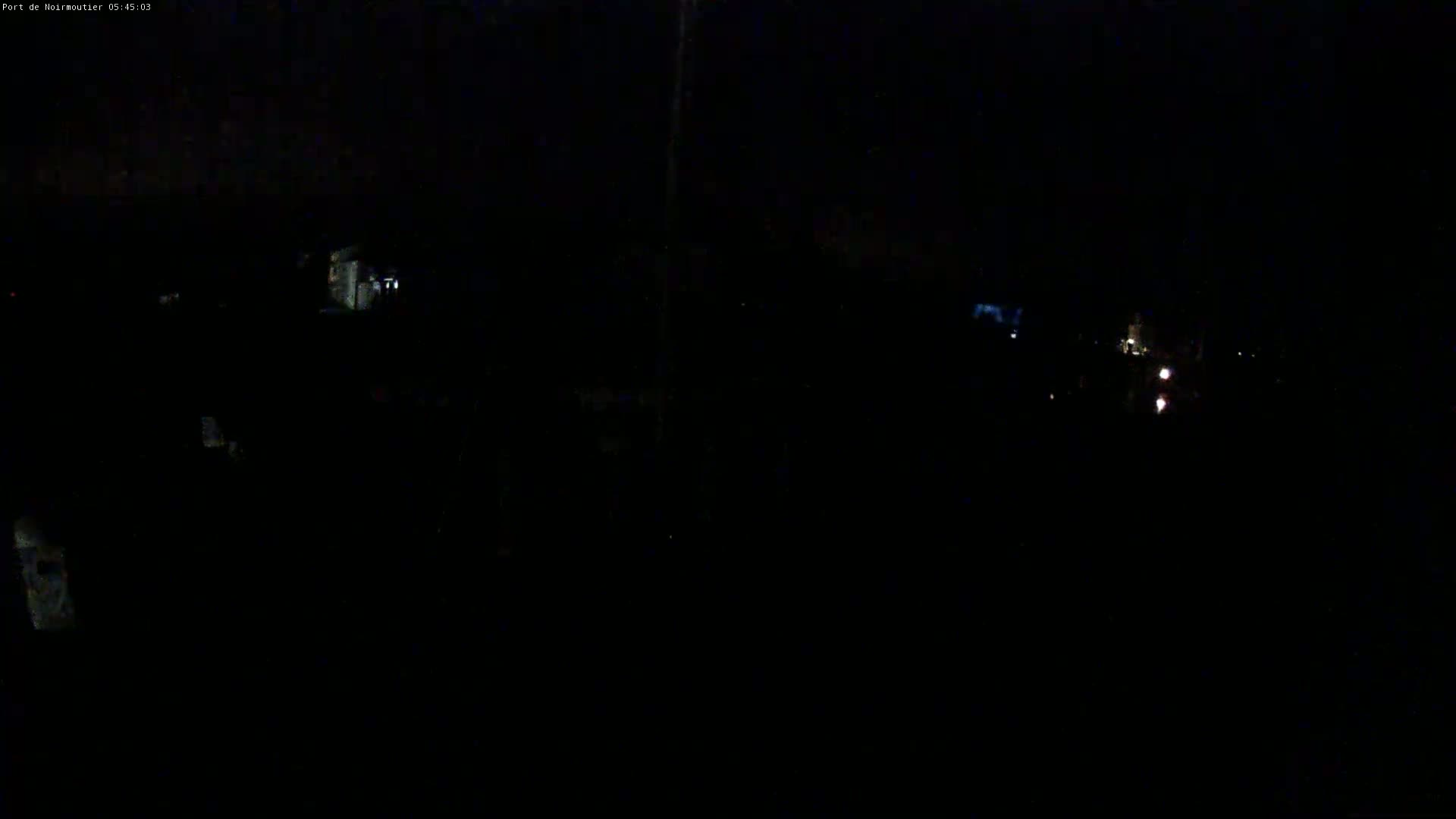 A dark, nighttime scene shows dimly lit buildings and faint lights in the distance under a mostly clear sky.