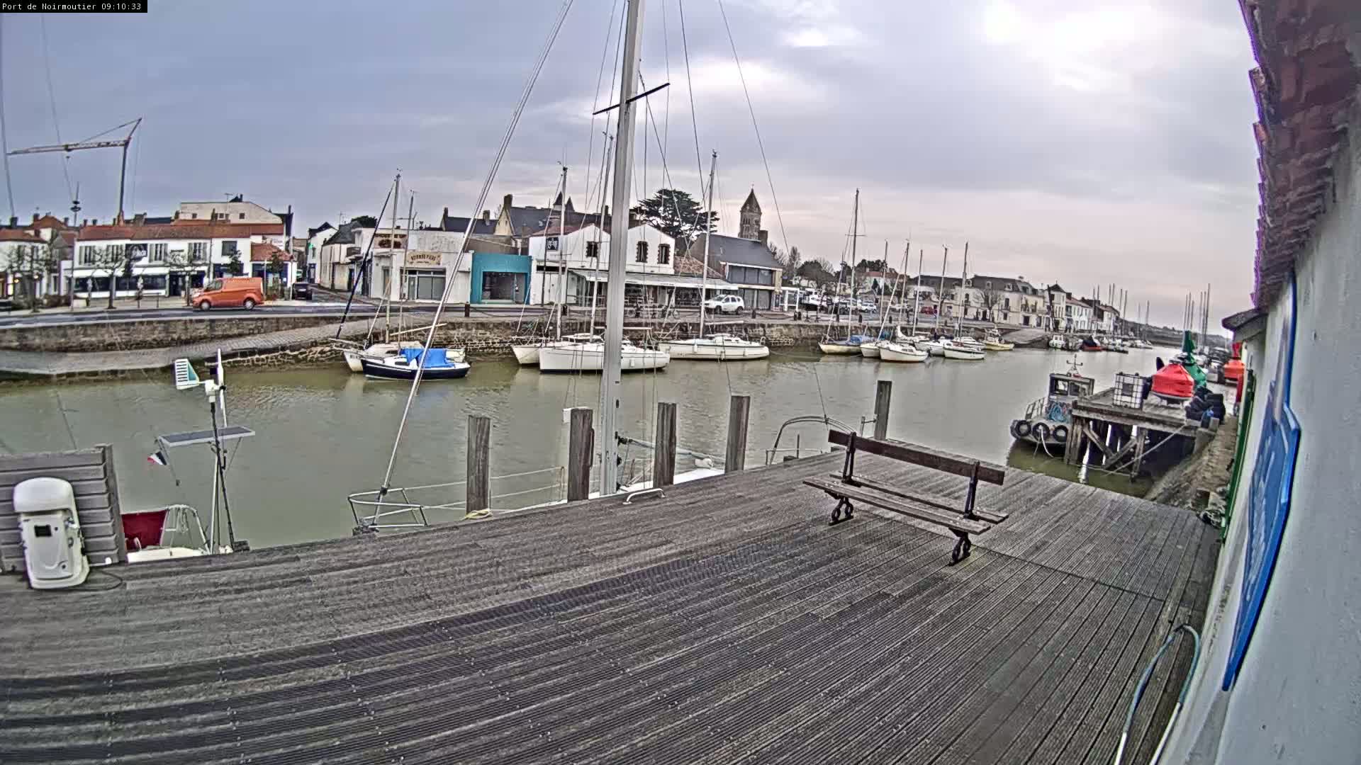 A harbor filled with sailboats under a cloudy sky, viewed from a wooden dock.