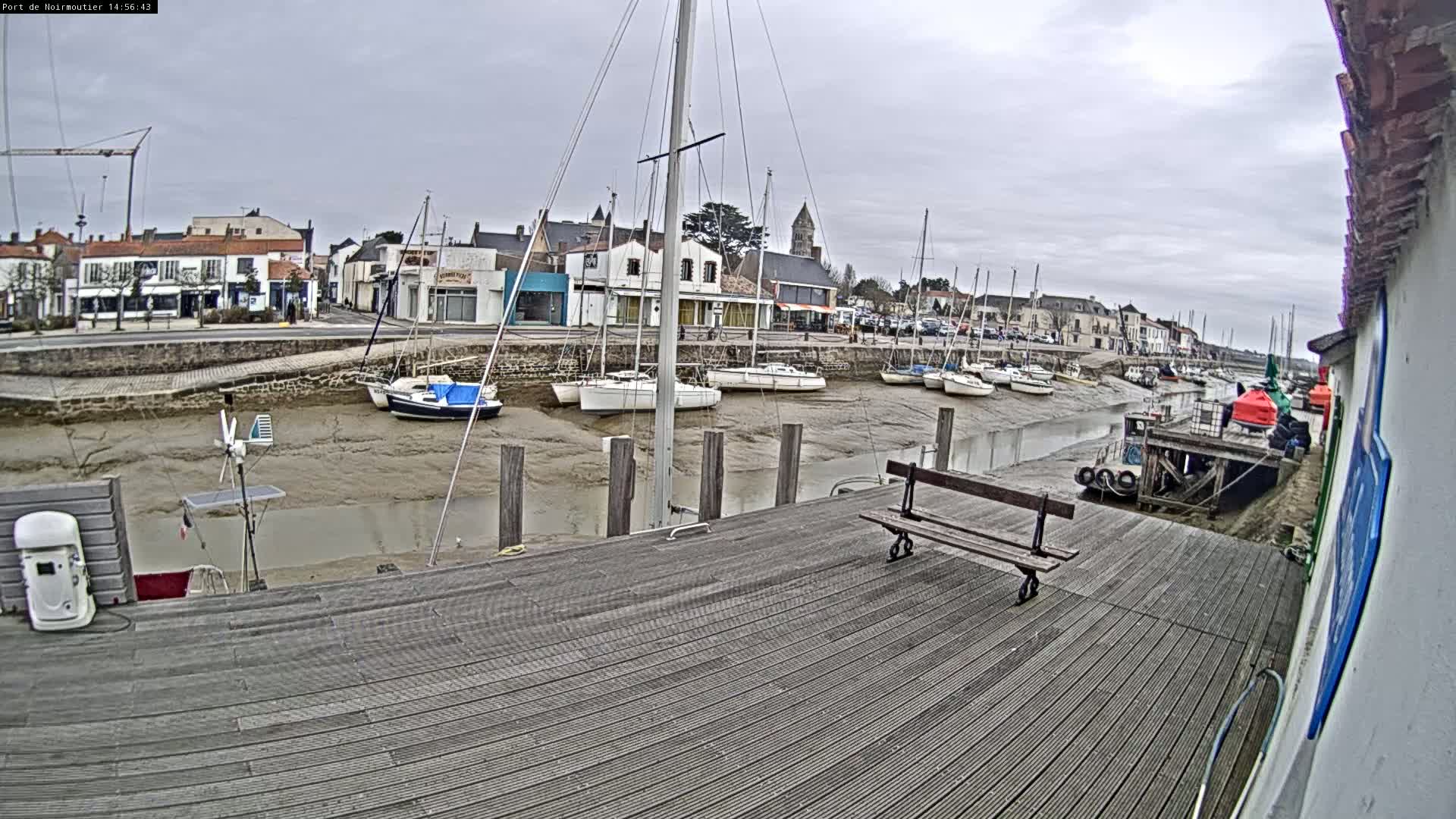 A wooden dock overlooks a harbor filled with sailboats at low tide under an overcast sky.