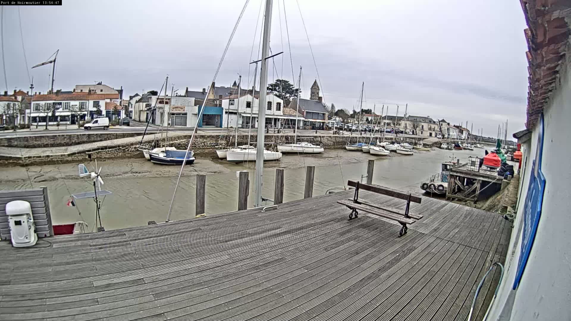 A wooden dock overlooks a calm harbor with several sailboats at low tide under an overcast sky.