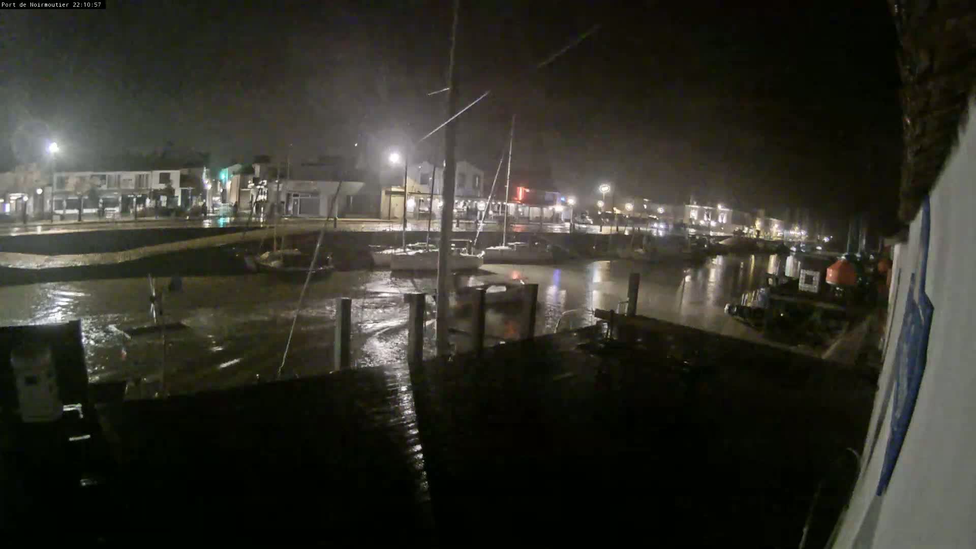 A nighttime view of a harbor with boats moored in turbulent water under heavy rain.