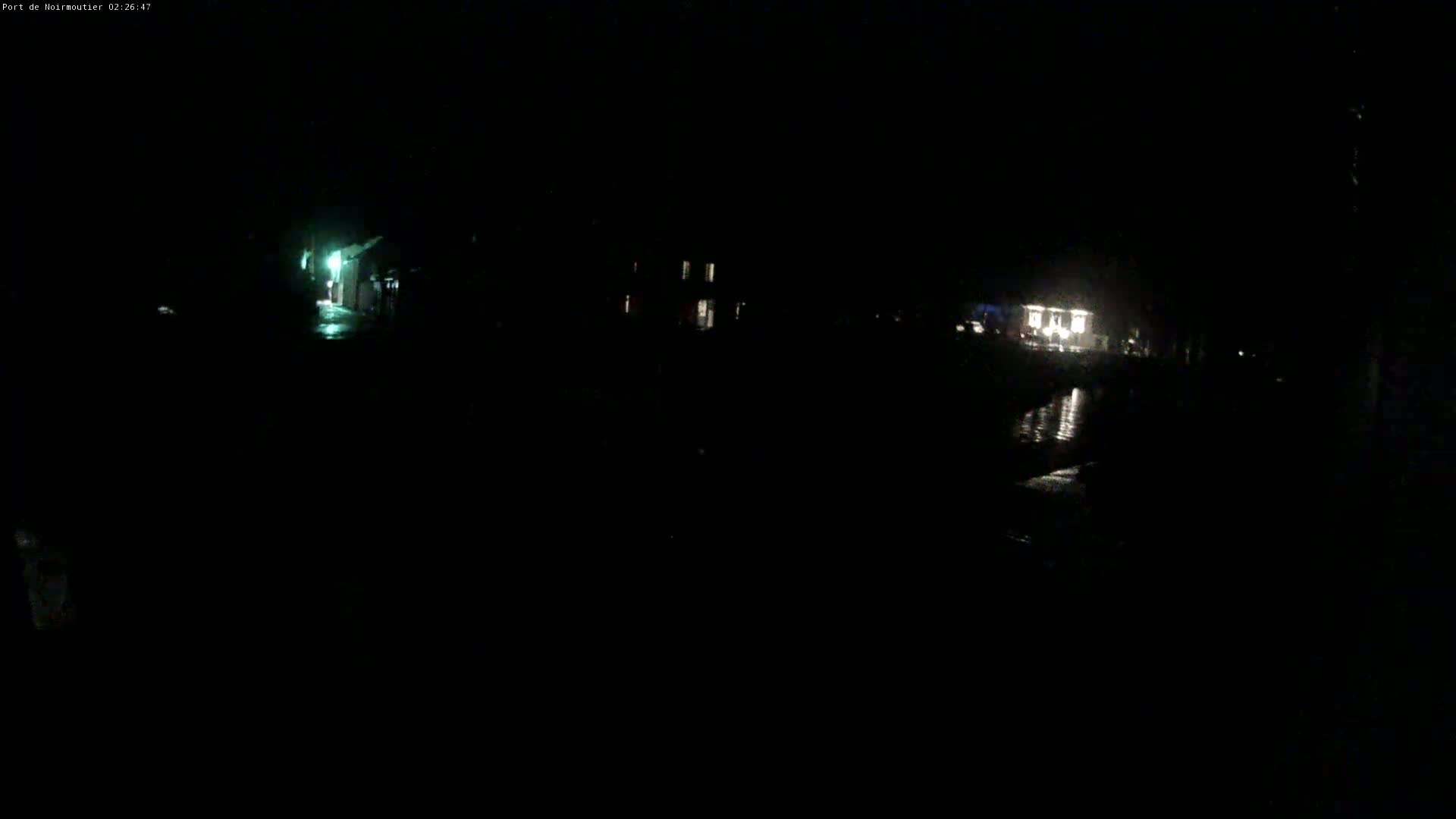 At night, dimly lit buildings and a wet, dark surface are visible under a dark sky.