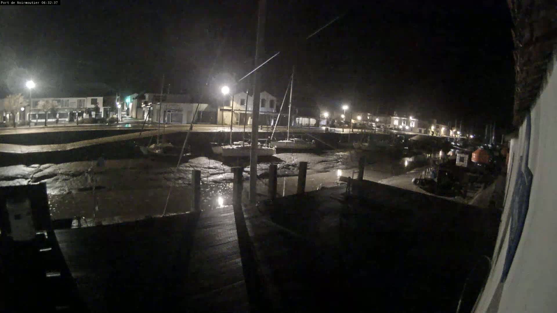 At night, a mostly empty harbor is seen at low tide, with several sailboats resting on the exposed mud and a dock in the foreground.