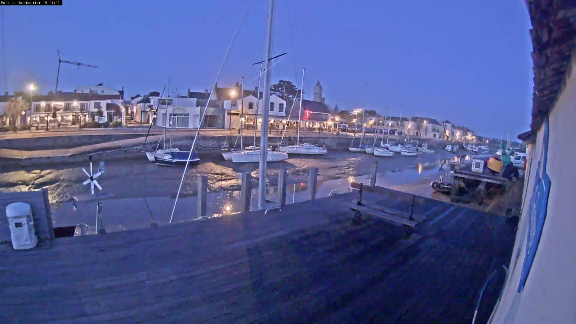A harbor at low tide under a twilight sky, with sailboats moored along a waterfront lined with buildings.