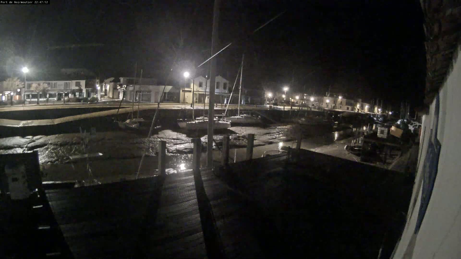 A nighttime view of a harbor at low tide, showing boats resting on exposed mudflats near a waterfront town illuminated by streetlights.
