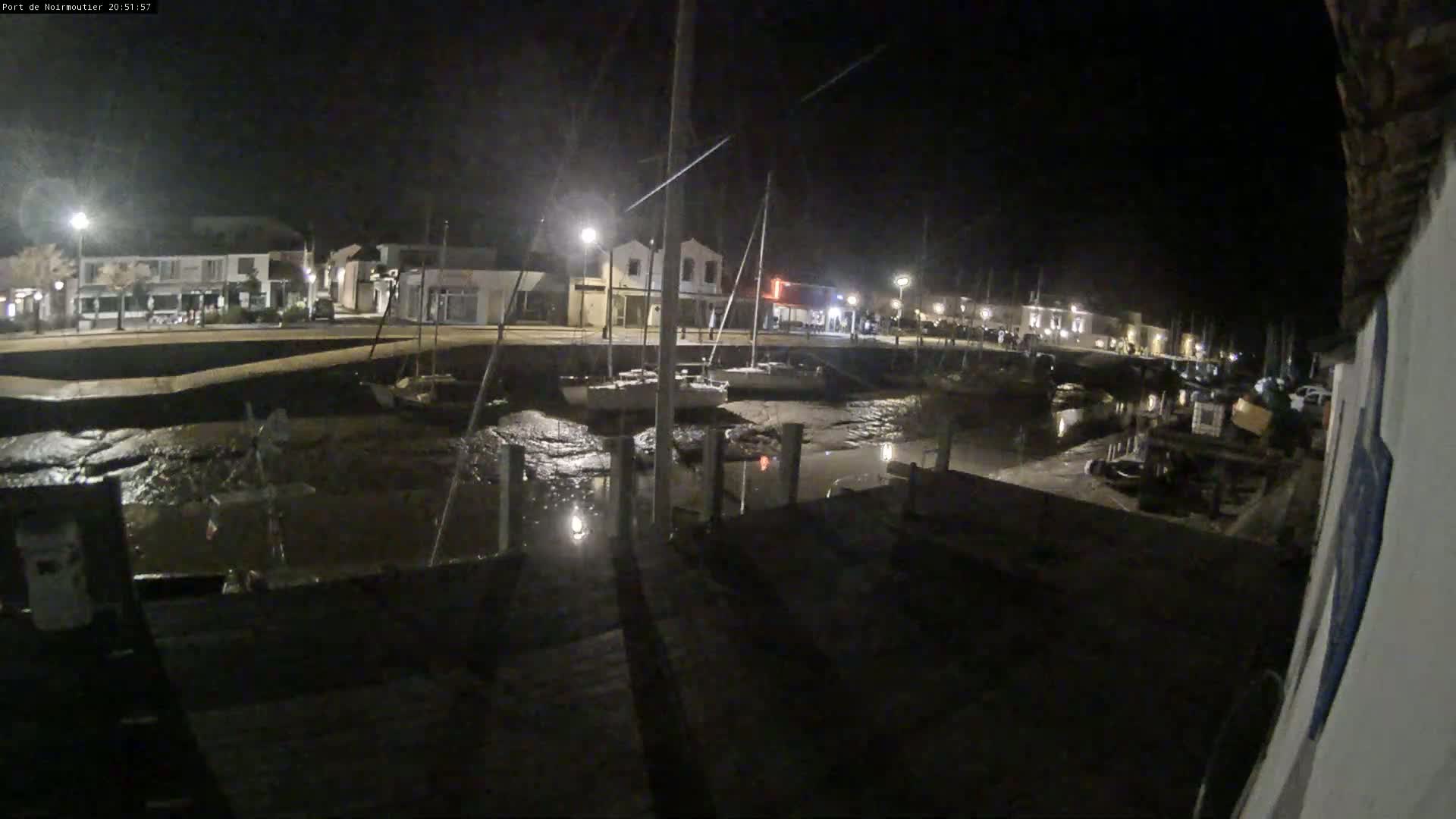 A nighttime view of a harbor with several boats moored at low tide, illuminated by streetlights along a waterfront.