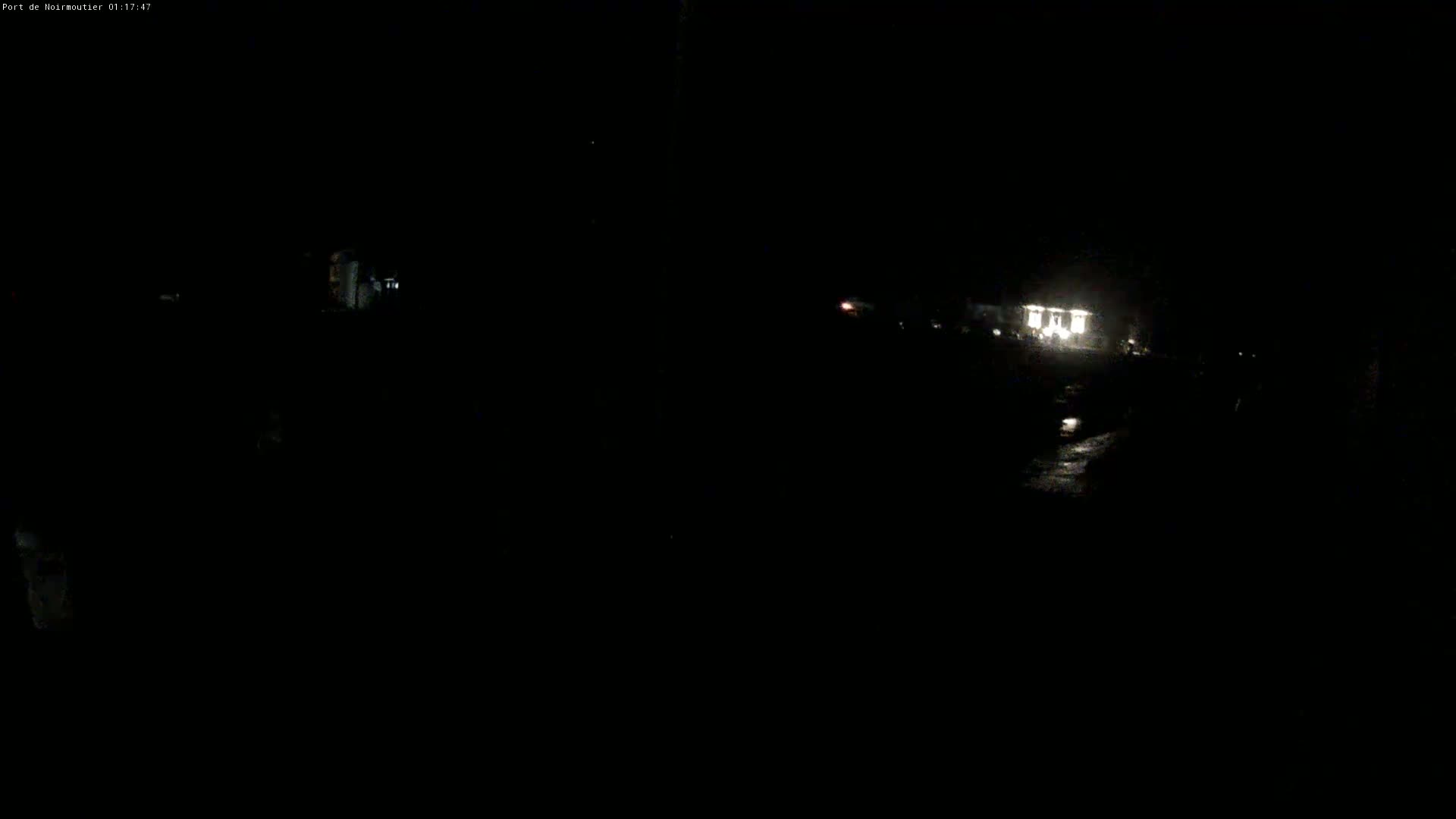 A dimly lit nighttime scene shows a building with lights on in the distance, under a dark sky.