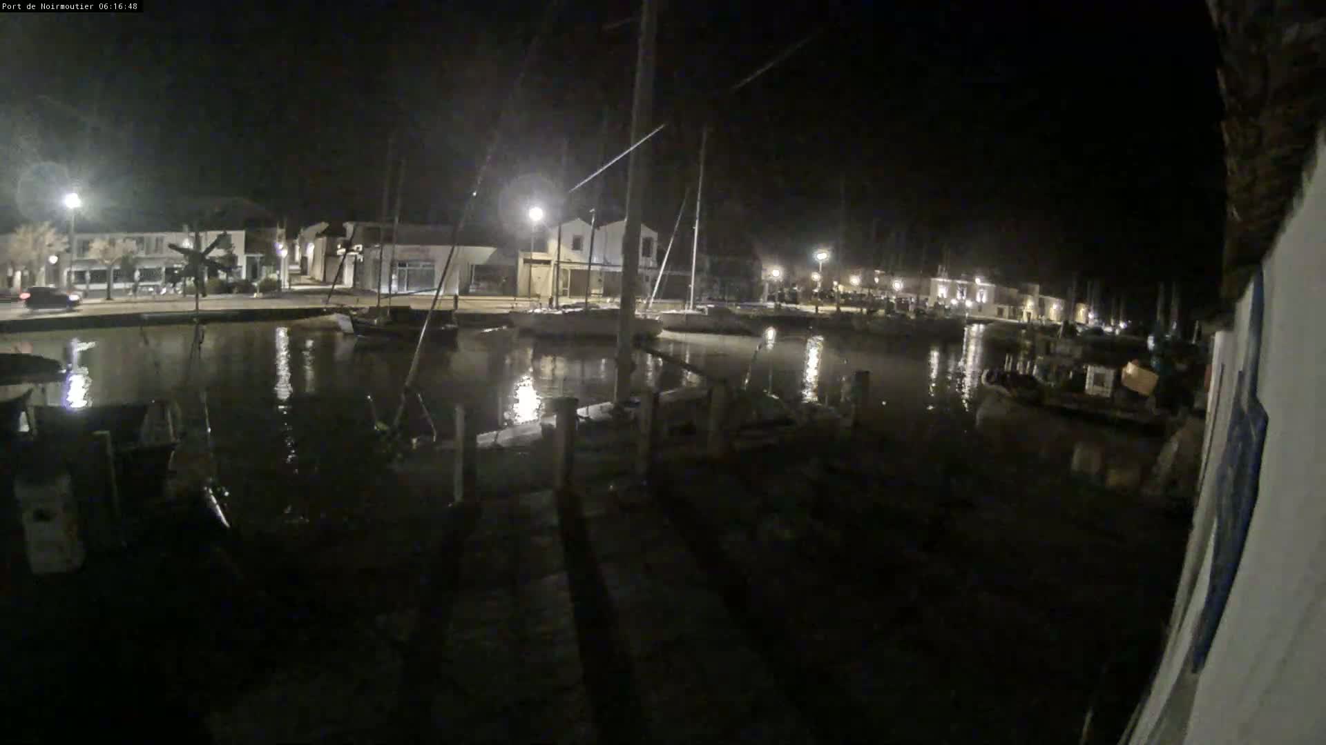 A nighttime view of a calm harbor with sailboats moored alongside a waterfront at night.