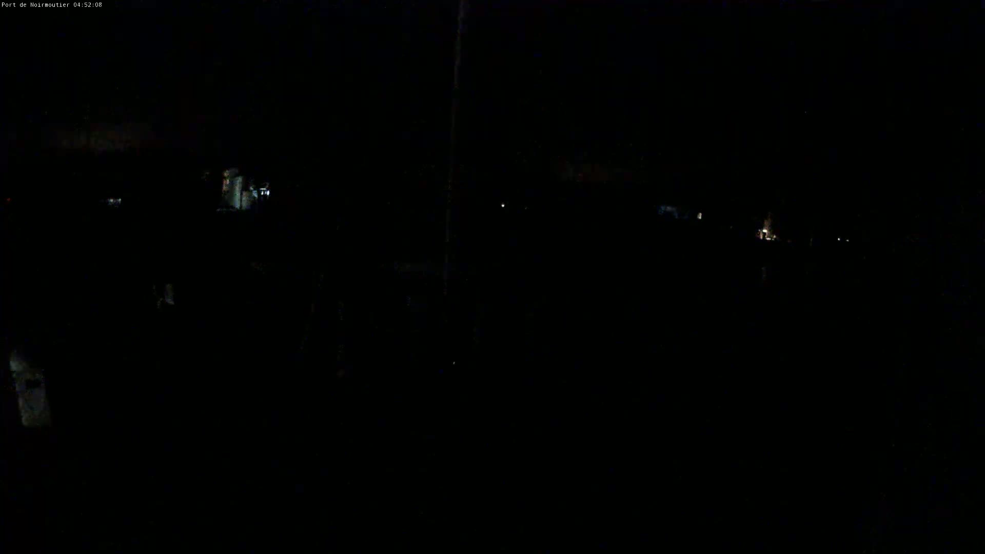 A nighttime, dark outdoor scene shows faintly illuminated structures and distant lights.