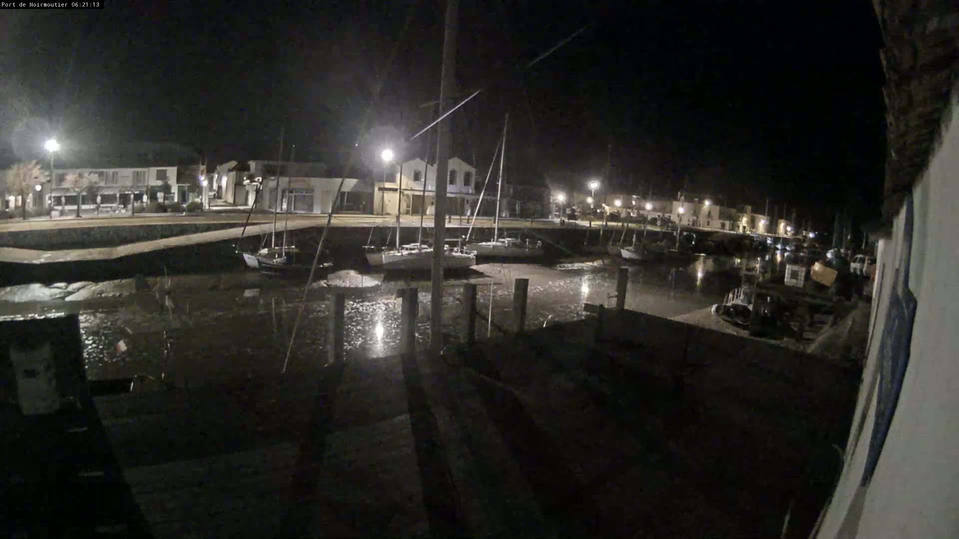 Several sailboats are moored in a calm, shallow harbor at night, under artificial lighting.