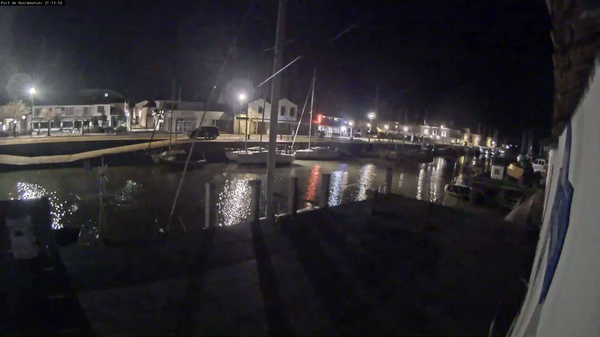 At night, a calm body of water reflects the lights of buildings and boats in a harbor.