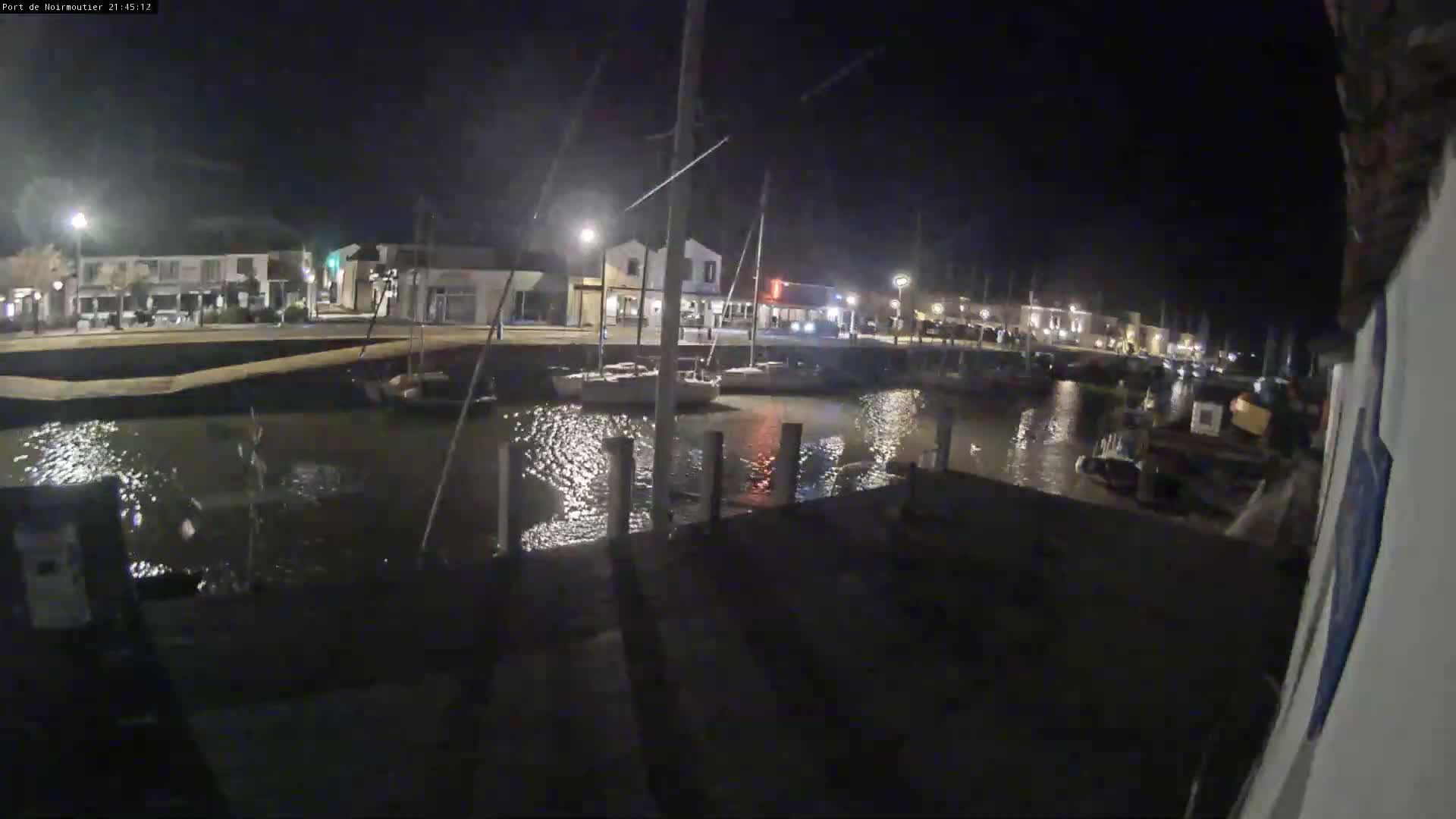 A nighttime view of a calm harbor with boats docked along a waterfront lined with buildings.
