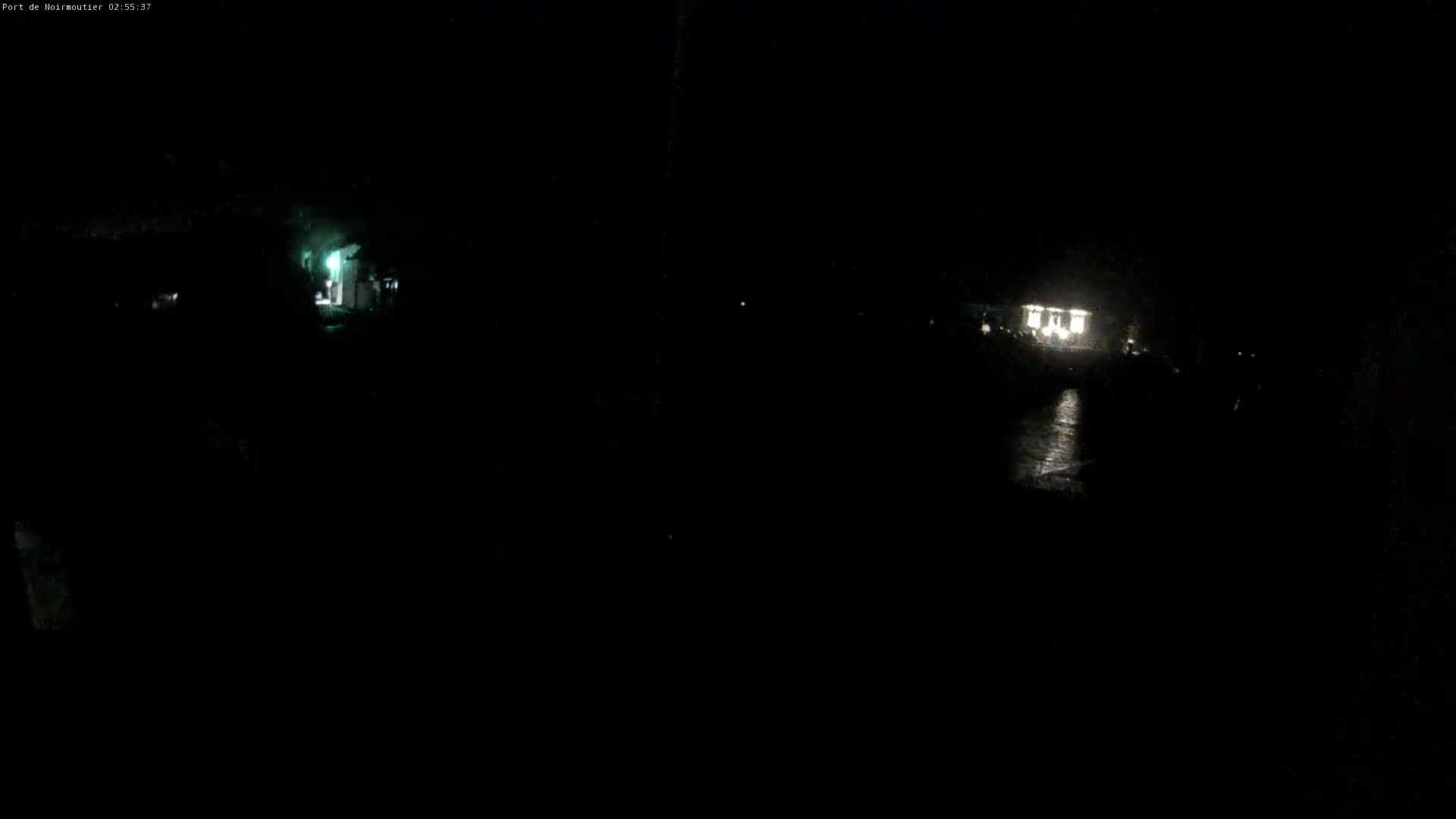 A dark, nighttime scene shows a dimly lit area with a few lights in the distance.