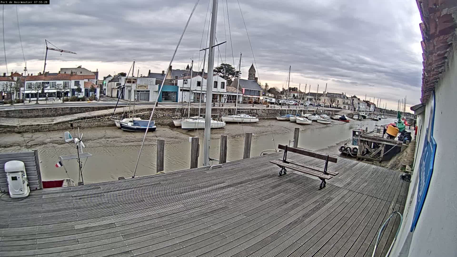A wooden dock overlooks a harbor with several sailboats at low tide under a cloudy sky.