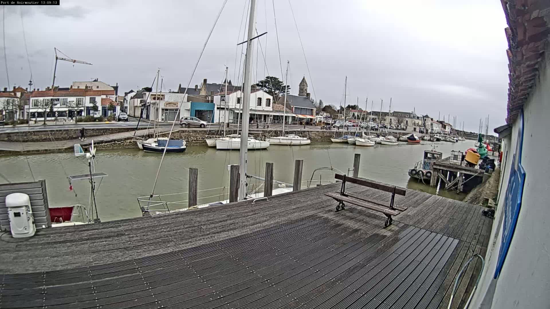 A harbor filled with sailboats under an overcast sky, viewed from a wooden dock with a bench.
