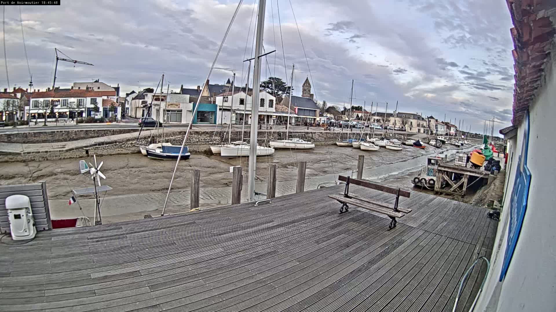 A wooden dock overlooks a harbor with several sailboats at low tide under a cloudy sky.