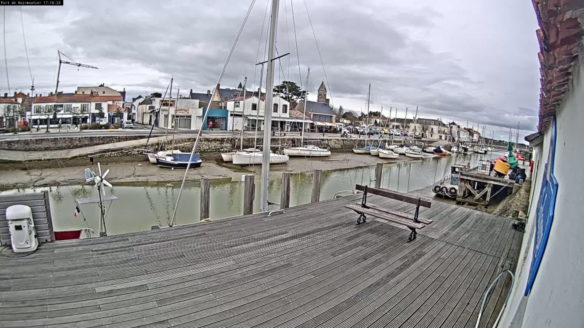A wooden dock overlooks a calm harbor with several sailboats at low tide under a cloudy sky.