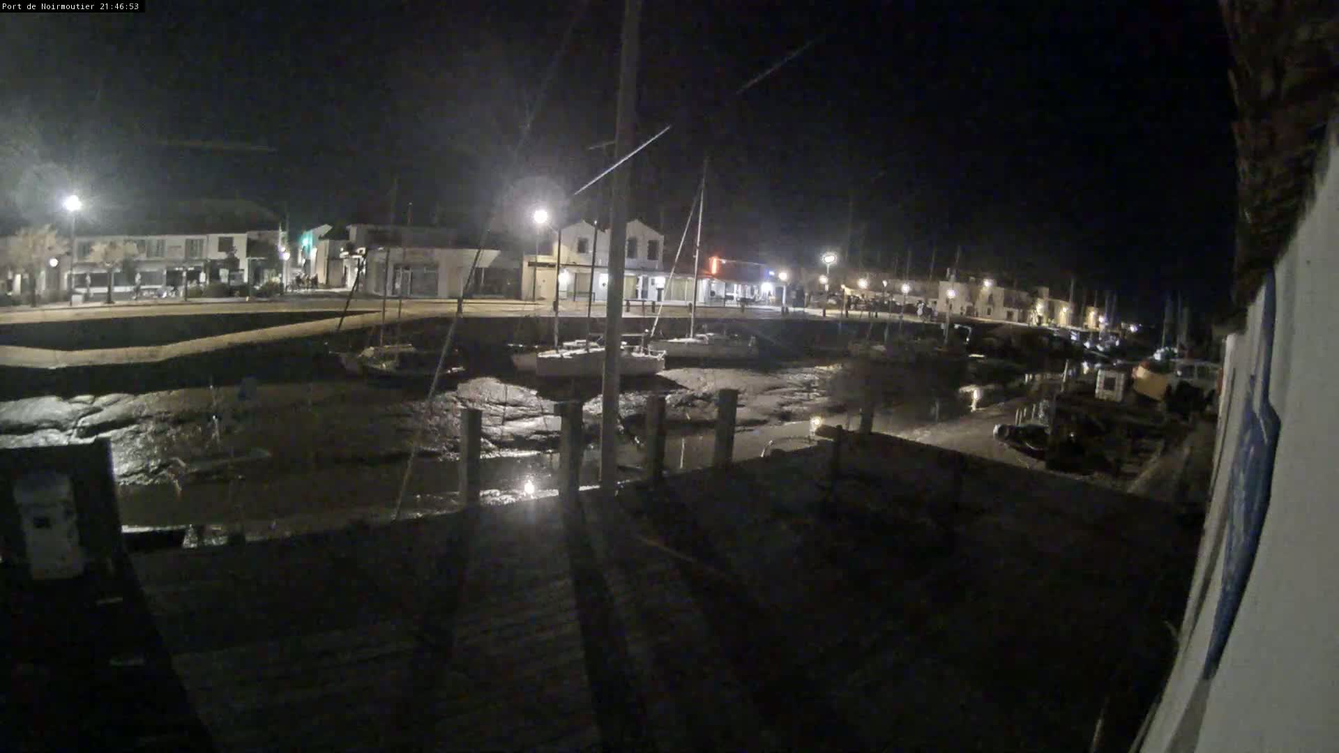 A nighttime view of a harbor with boats docked, low tide exposing mudflats, and buildings lit along the waterfront.