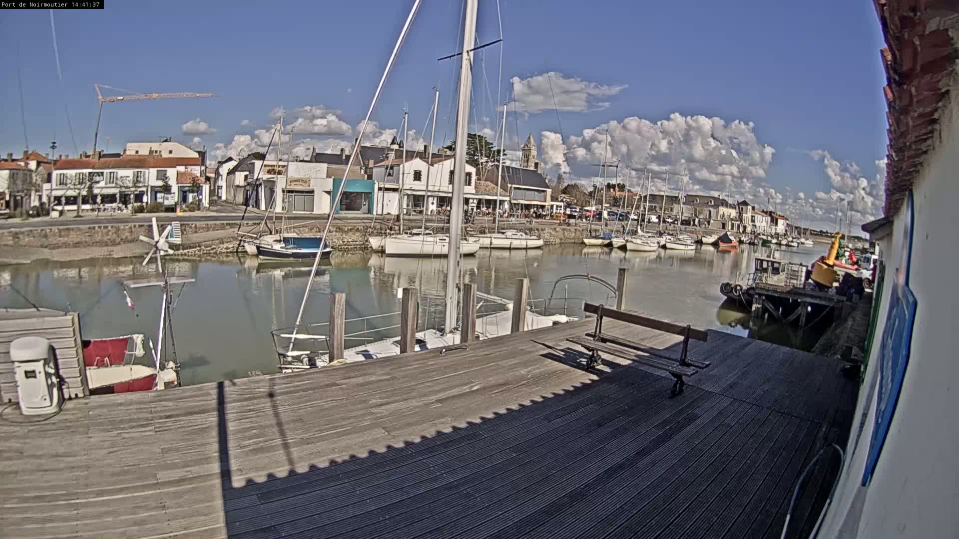 A wooden dock overlooks a calm harbor filled with sailboats under a partly cloudy sky.