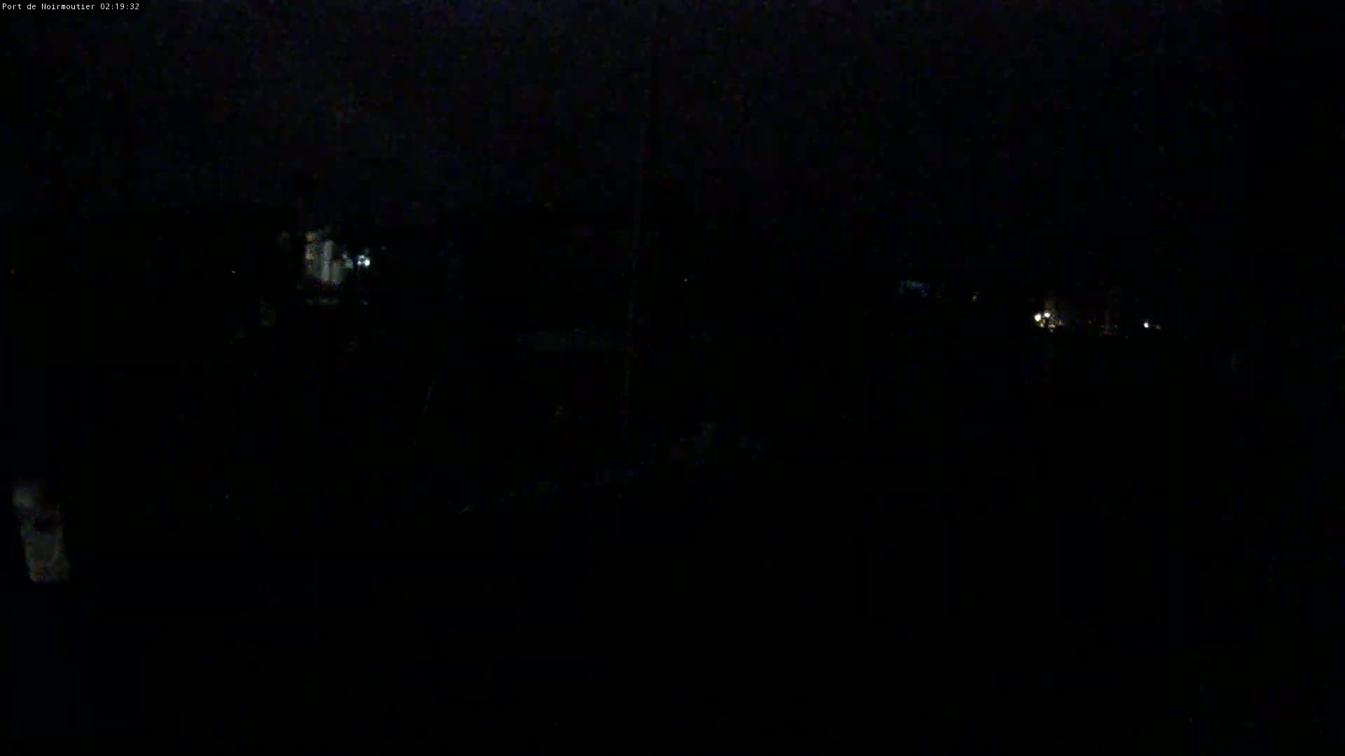 A very dark, nighttime outdoor scene shows a few faint lights in the distance under a cloudy sky.