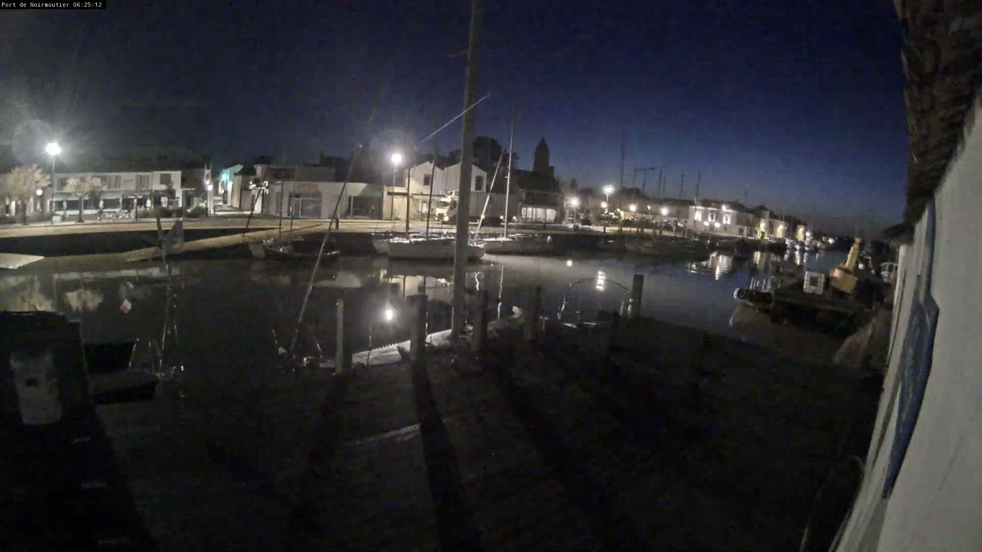 A nighttime view of a calm harbor with docked boats and buildings lining the waterfront under a dark blue sky.