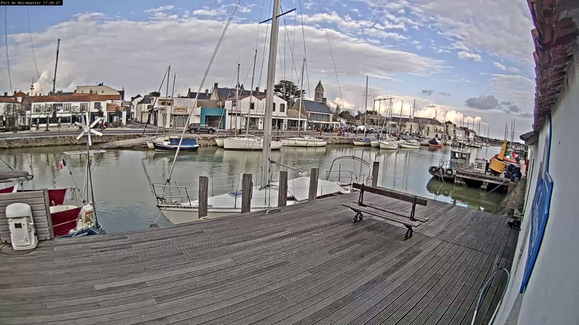 A harbor filled with sailboats and small motorboats under a partly cloudy sky, viewed from a wooden dock.