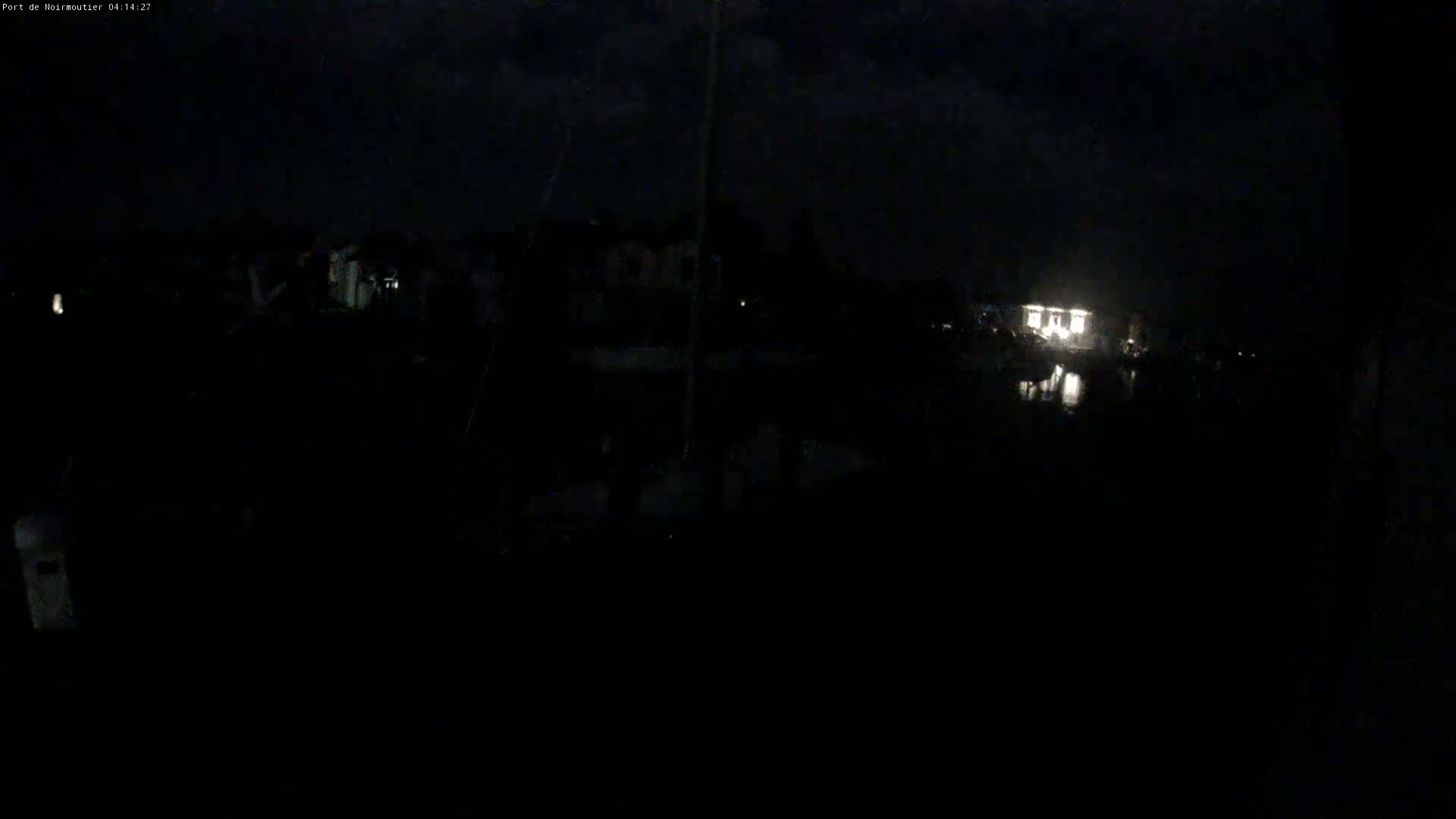A nighttime, dark view of a waterfront area with dimly lit buildings and a reflection of light on the water.