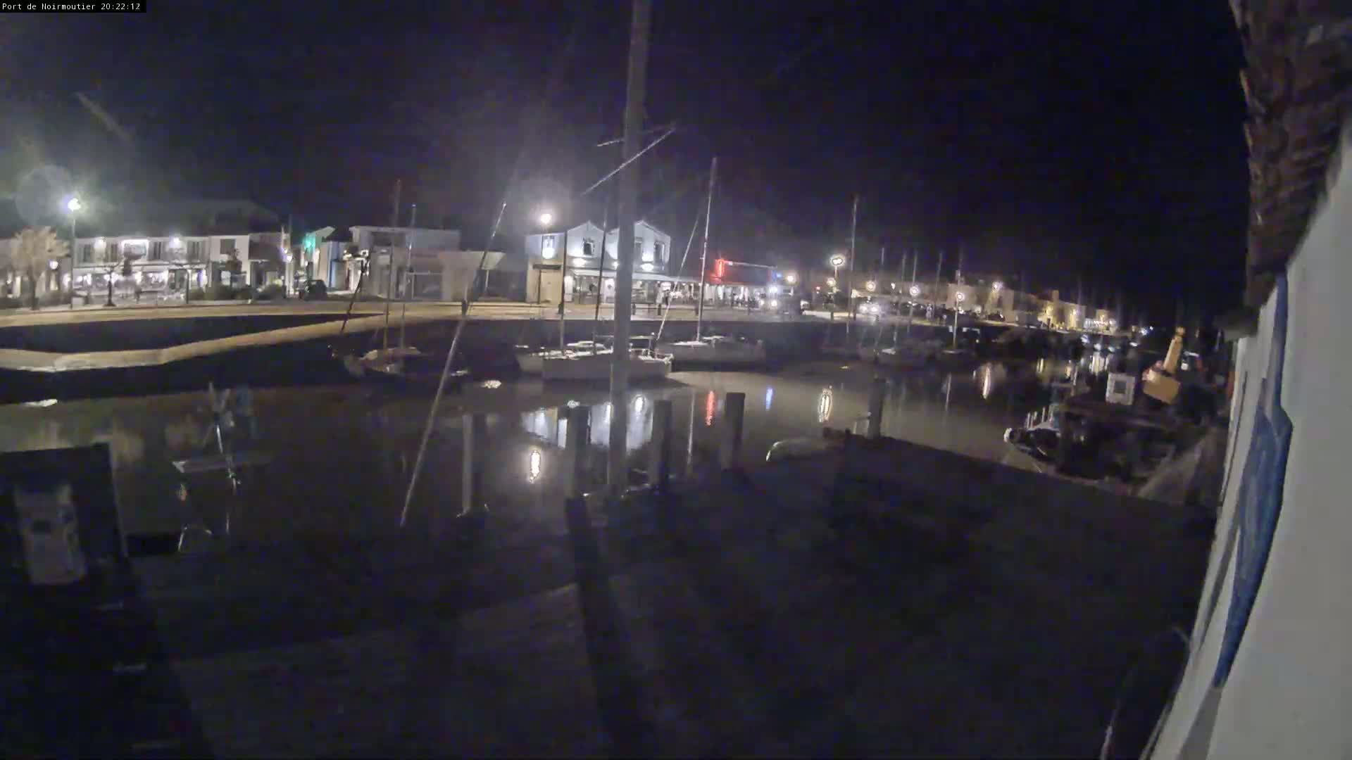 A nighttime view of a calm harbor with sailboats docked along a waterfront lined with buildings.