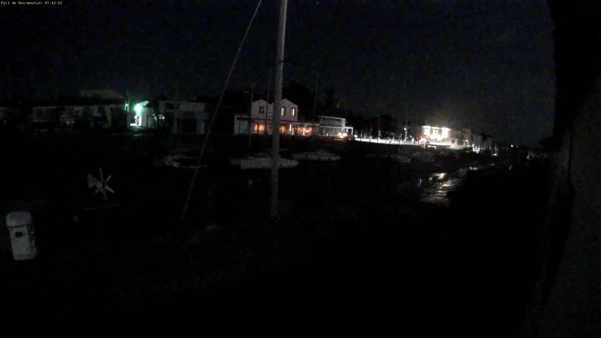 At night, a dark waterfront scene shows several boats moored near lit buildings.
