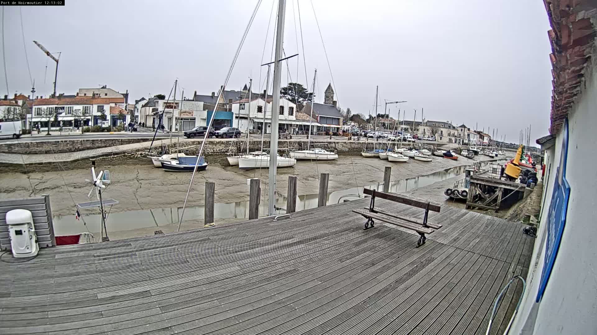 A wooden dock overlooks a harbor with numerous sailboats at low tide under an overcast sky.
