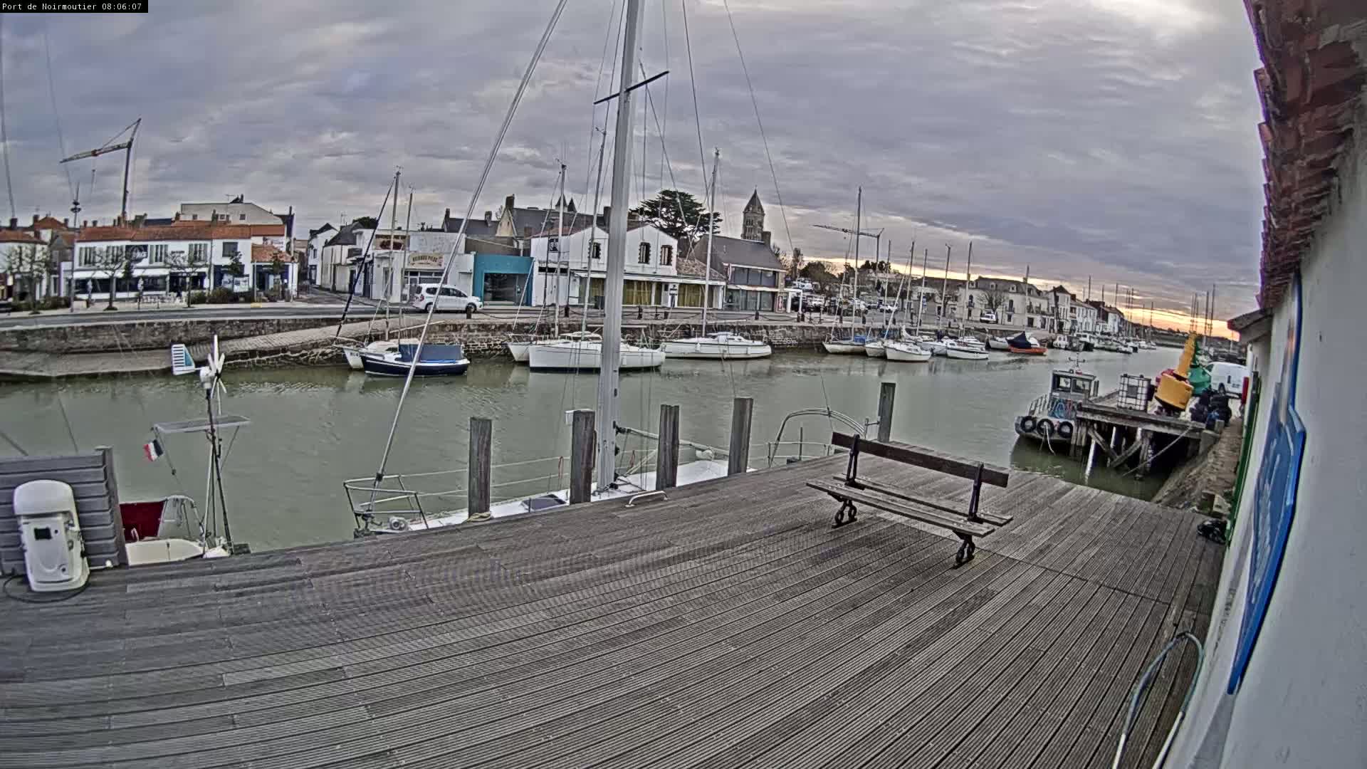 A wooden dock overlooks a calm harbor filled with sailboats under a cloudy sky.