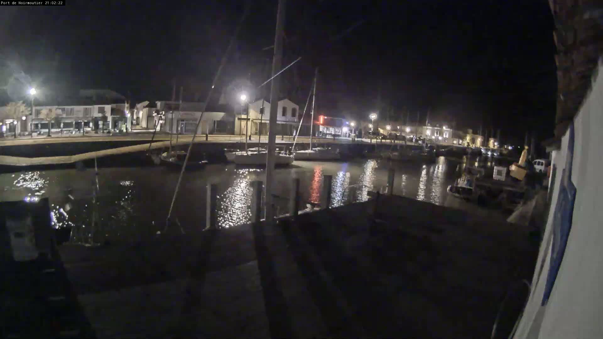 A nighttime view of a calm harbor with boats docked, illuminated by streetlights along a waterfront building.