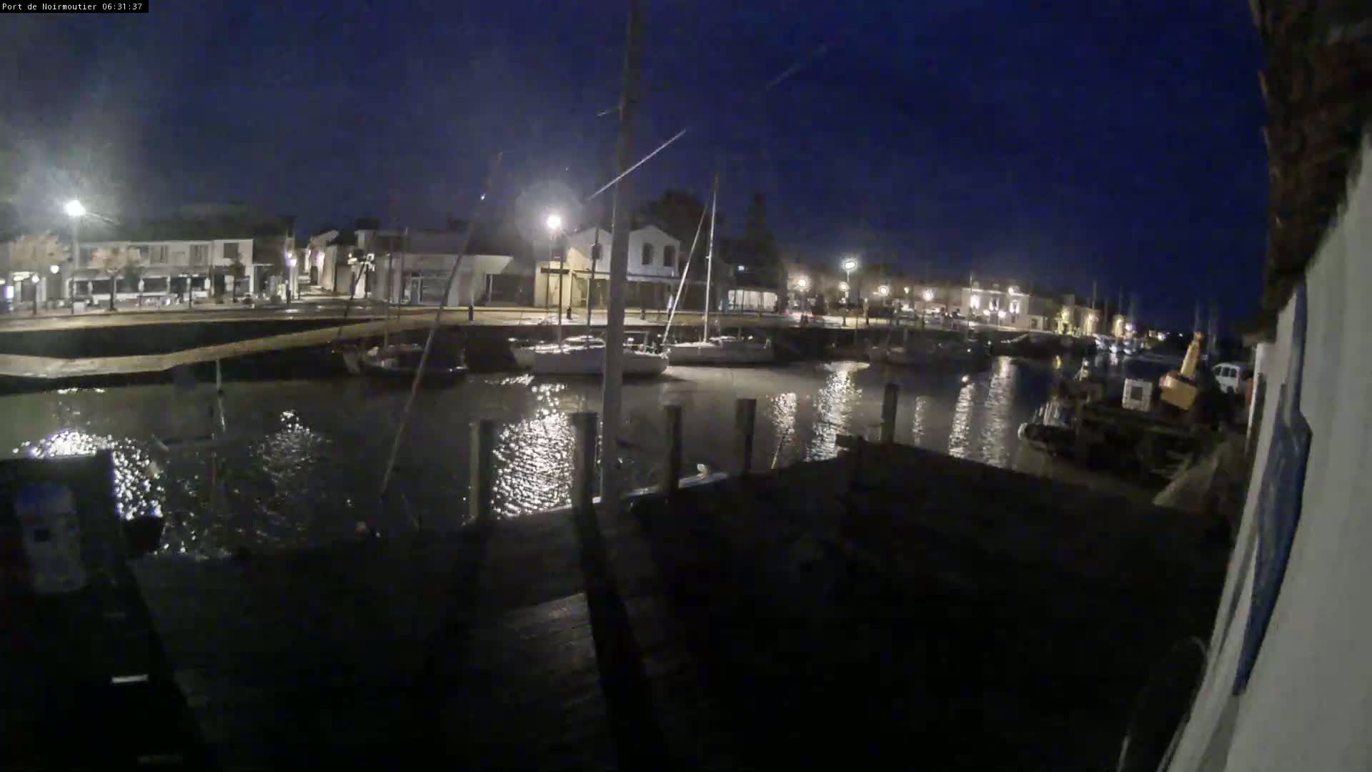 A nighttime view of a harbor with boats docked alongside a waterfront town under a clear, dark sky.