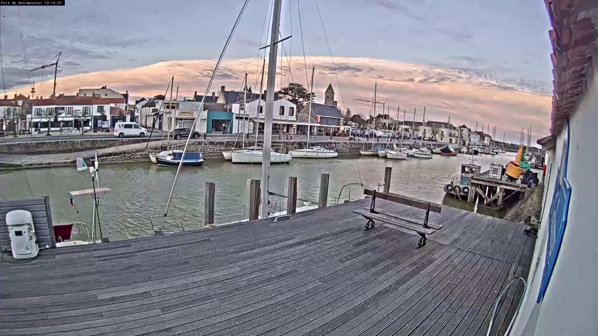 A wooden dock overlooks a calm harbor filled with sailboats under a partly cloudy, dusky sky.