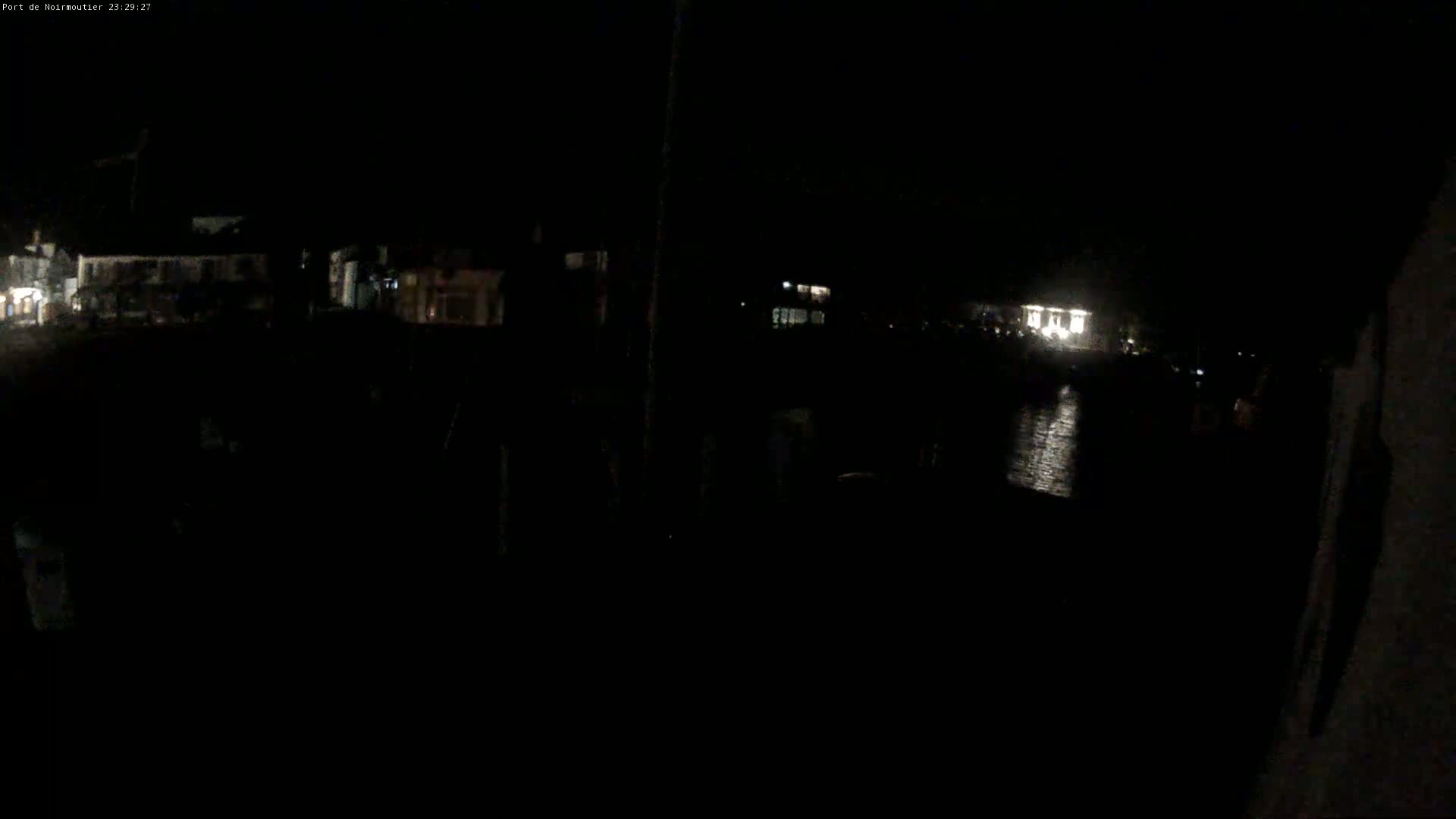 A nighttime, low-light view of a waterfront area with dimly lit buildings and a dark body of water reflecting some light.