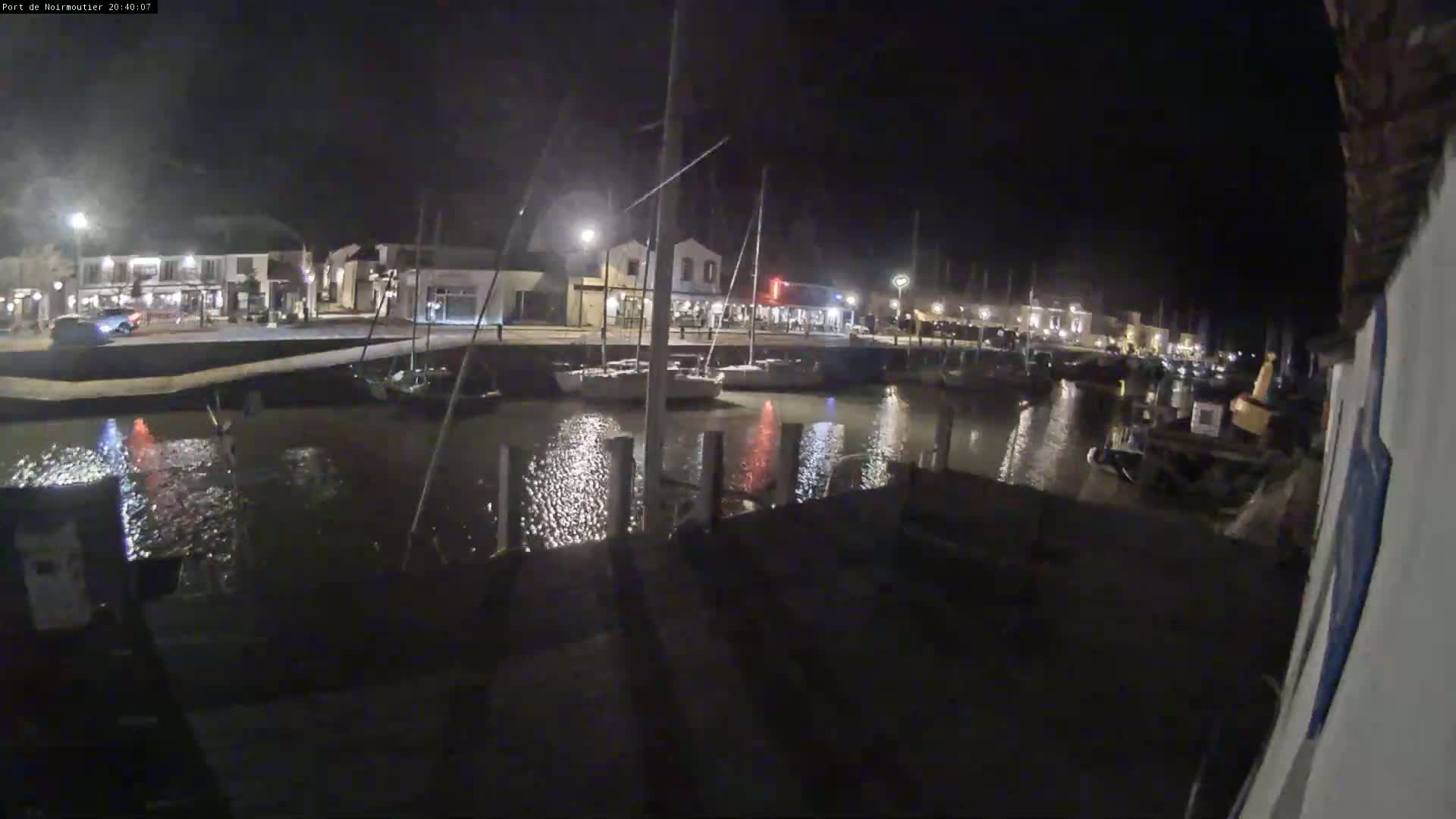 A nighttime view of a calm harbor with boats docked along a waterfront lined with buildings.