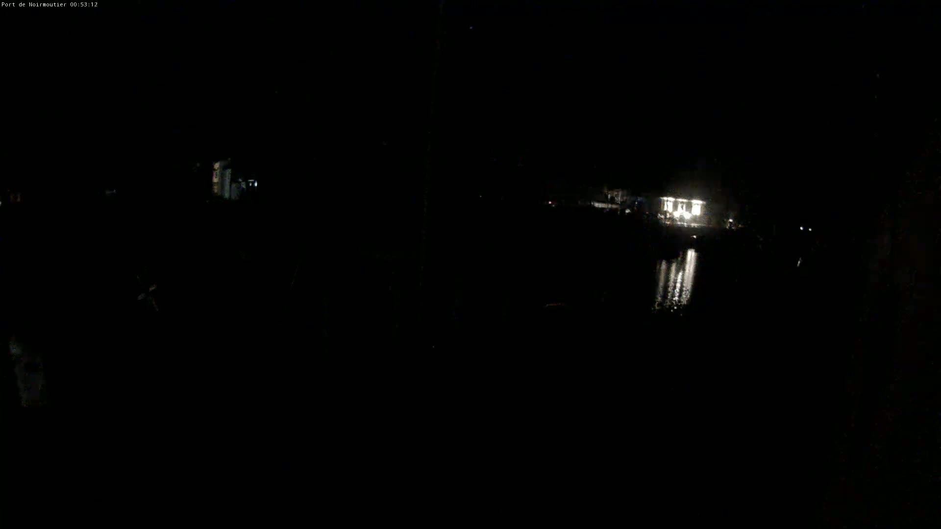 A dimly lit nighttime scene shows a body of water reflecting light from a building in the distance.