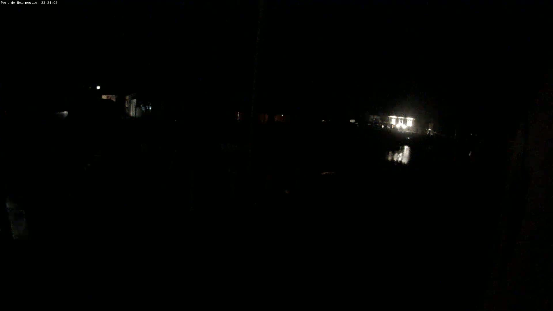 A dimly lit nighttime scene shows a body of dark water reflecting a brightly lit building in the distance.