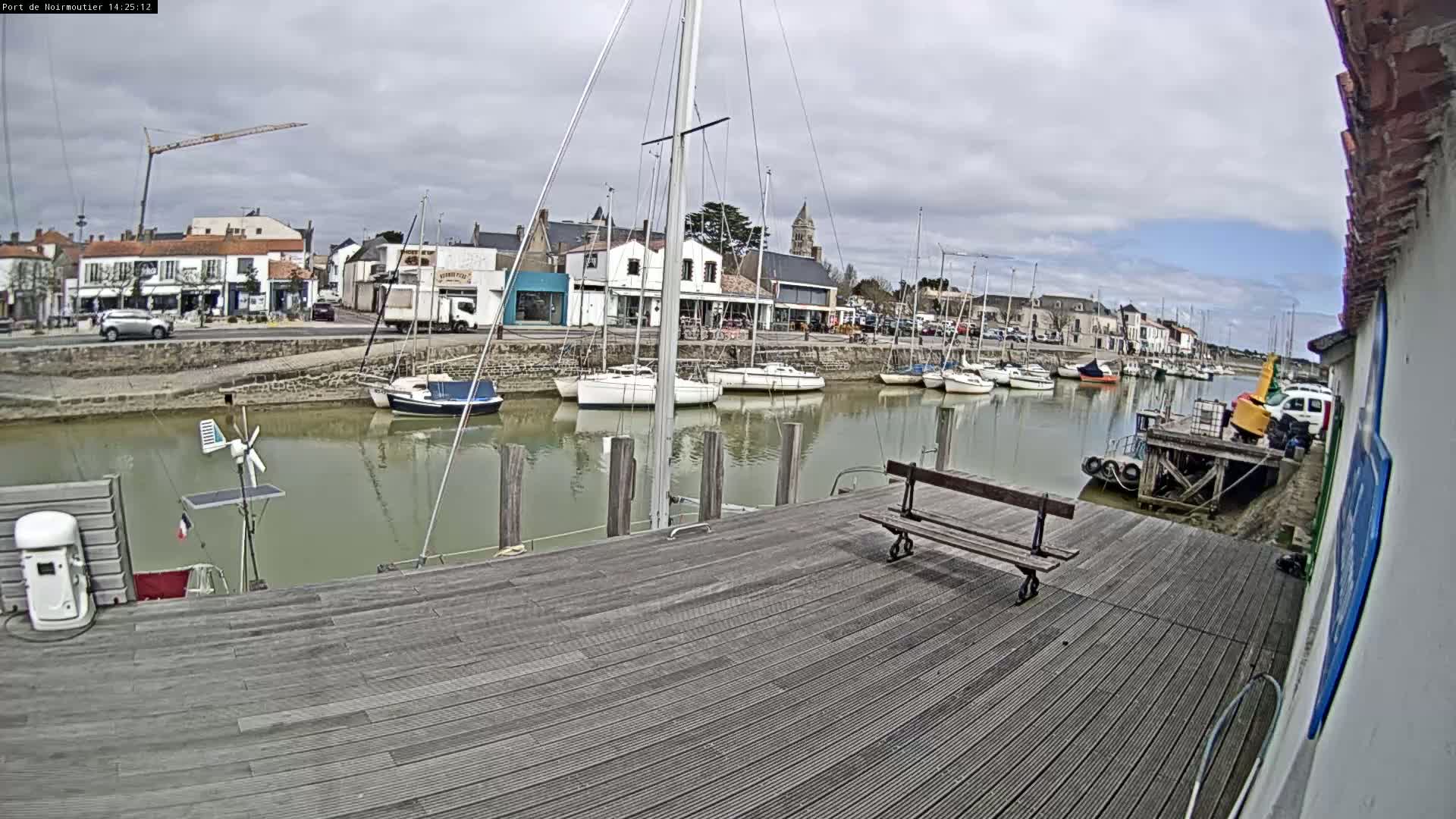 A wooden dock overlooks a calm harbor filled with sailboats on a cloudy day.