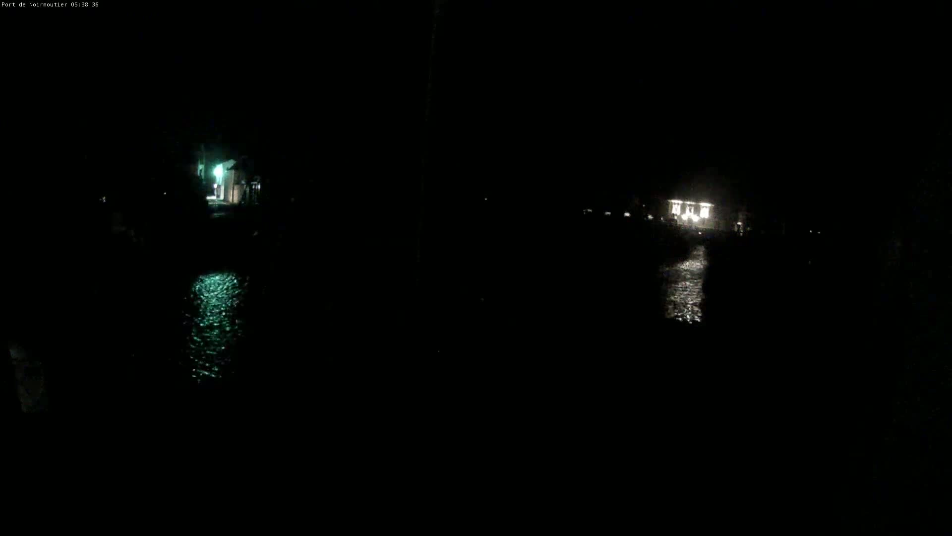 A dark nighttime scene shows a body of water reflecting dim lights from buildings in the distance.